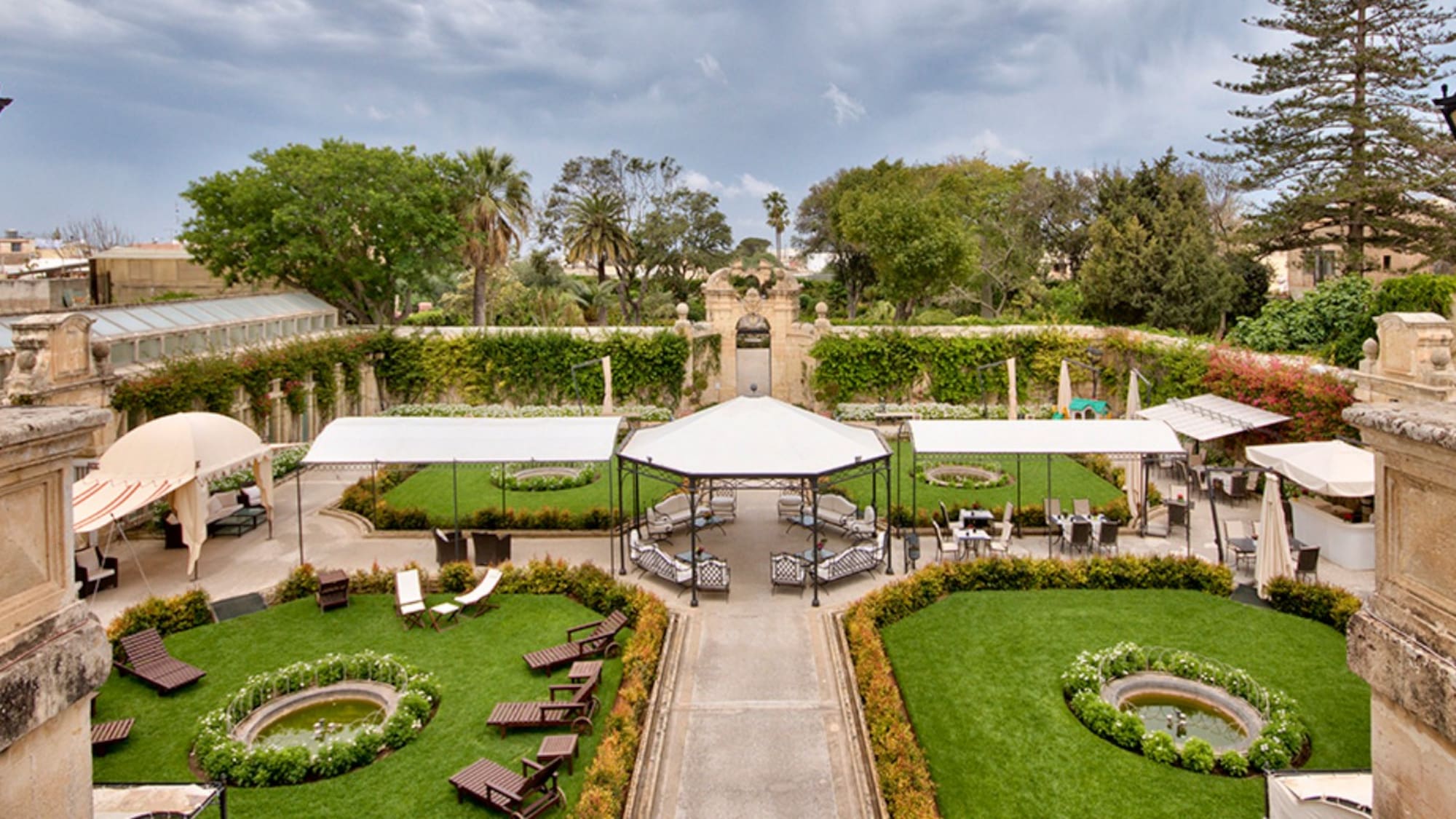 Lush resort garden courtyard with white pergolas, outdoor seating, and fountains.