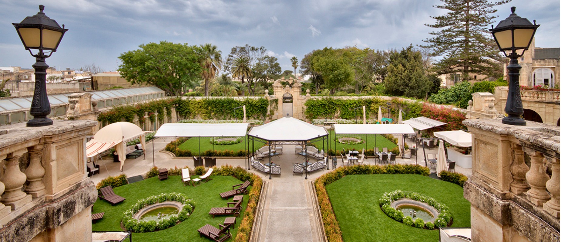 Lush resort garden courtyard with white pergolas, outdoor seating, and fountains.