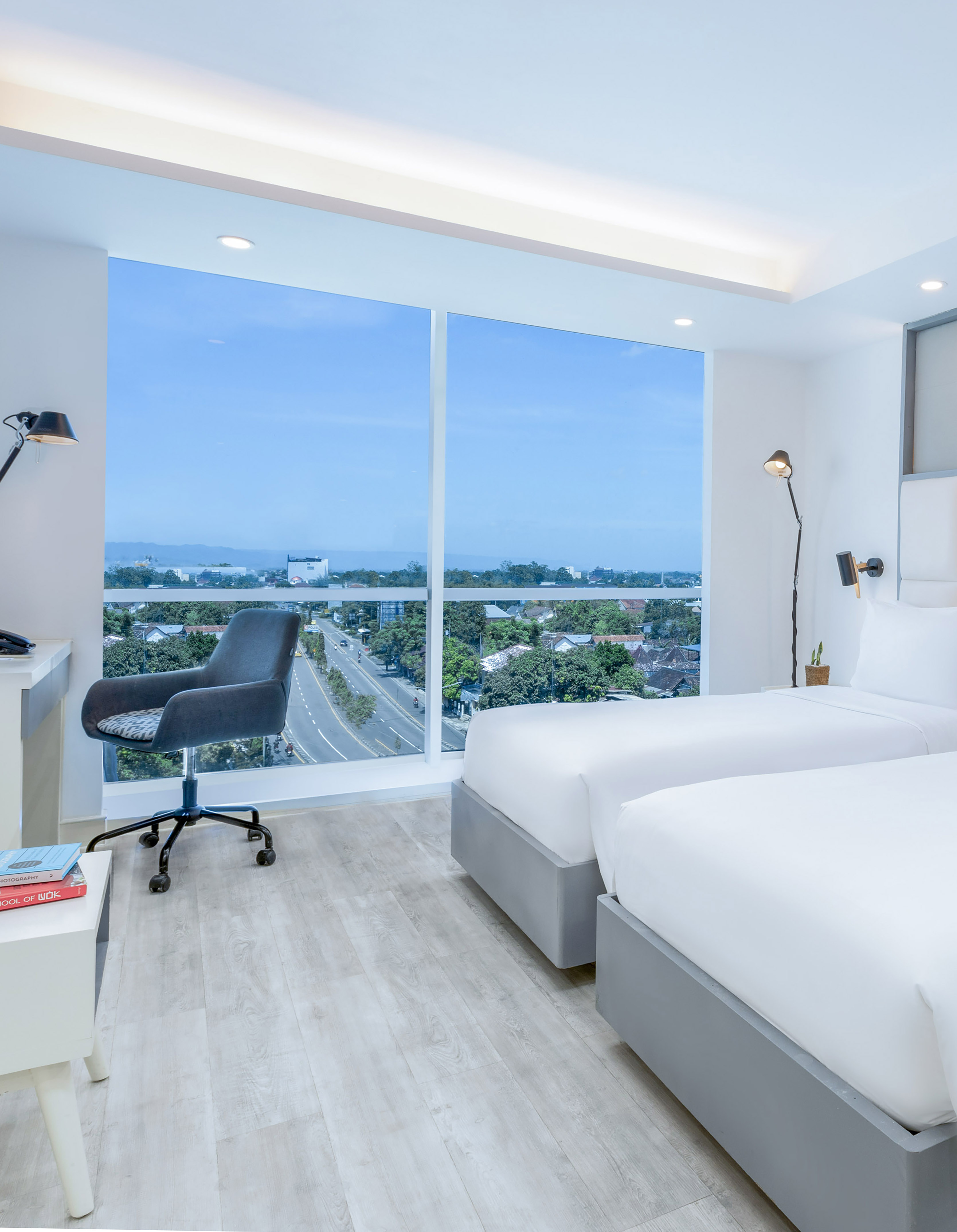 Modern hotel room with twin beds, work desk, and panoramic city view window.
