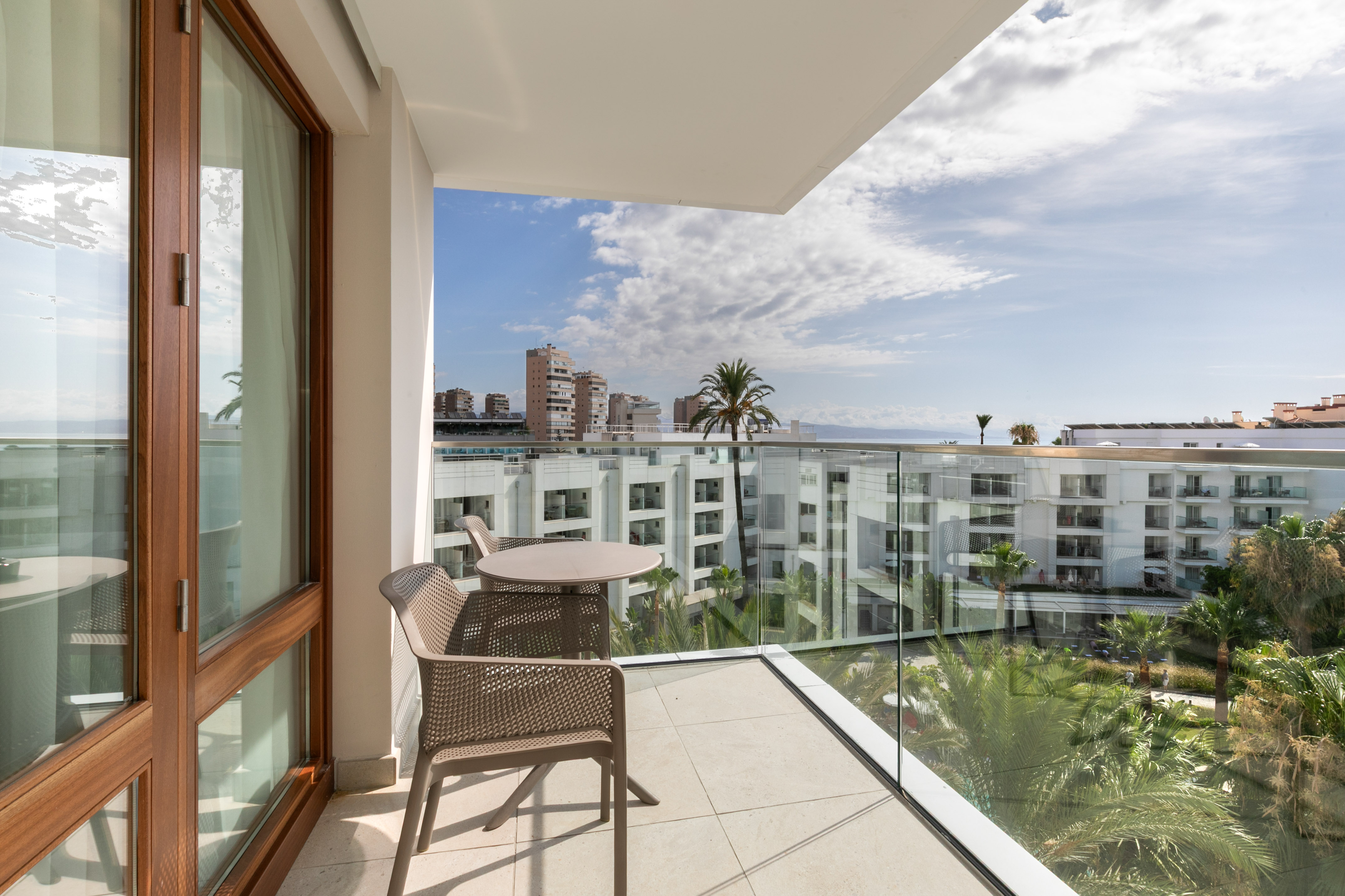 Modern hotel balcony with ocean view, palm trees, and outdoor seating.