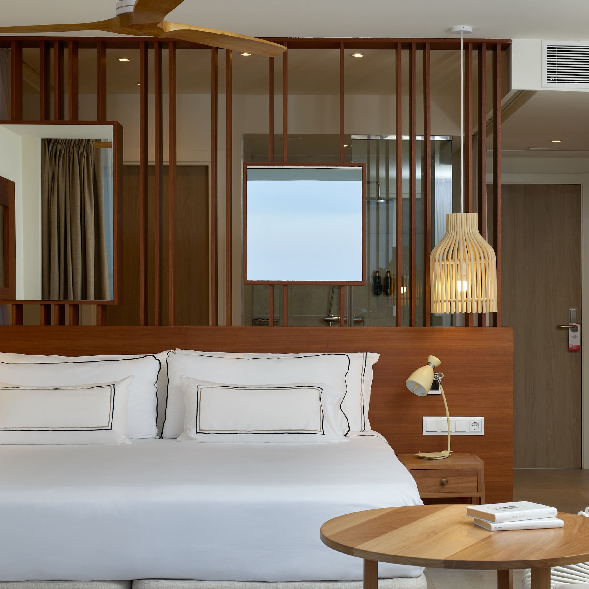 a bed with white sheets and a table in front of a room with a fan