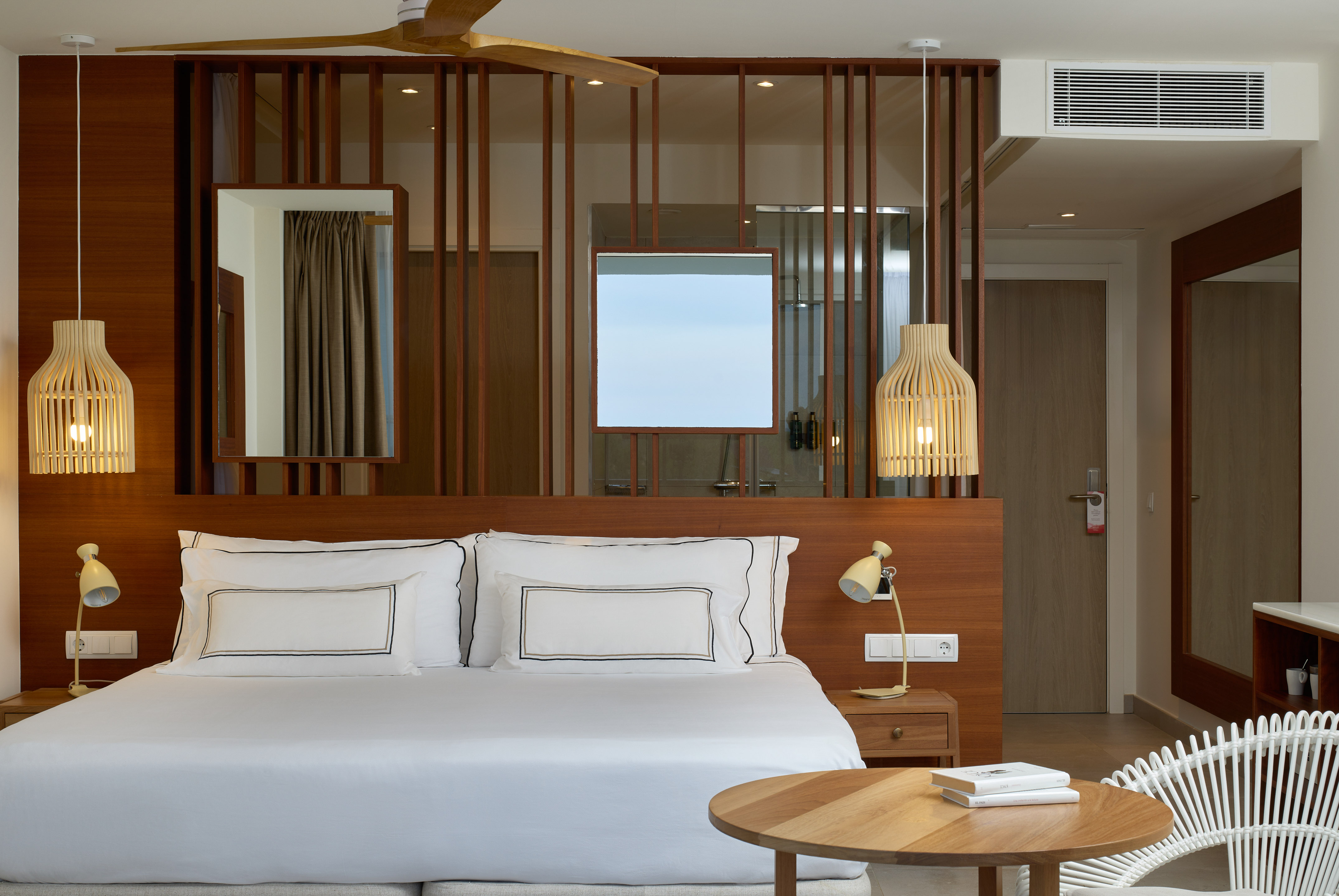 a bed with white sheets and a table in front of a room with a fan