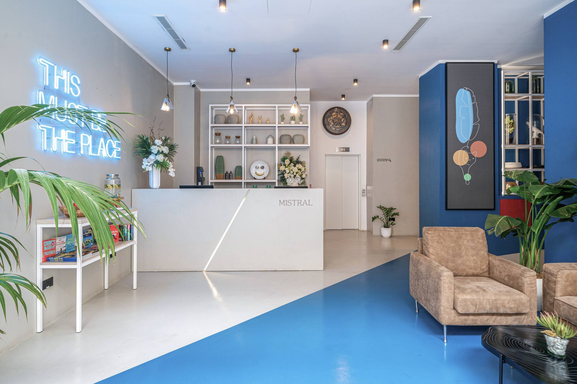 Stylish hotel lobby reception with "MISTRAL" desk, blue neon sign, and vibrant modern decor.