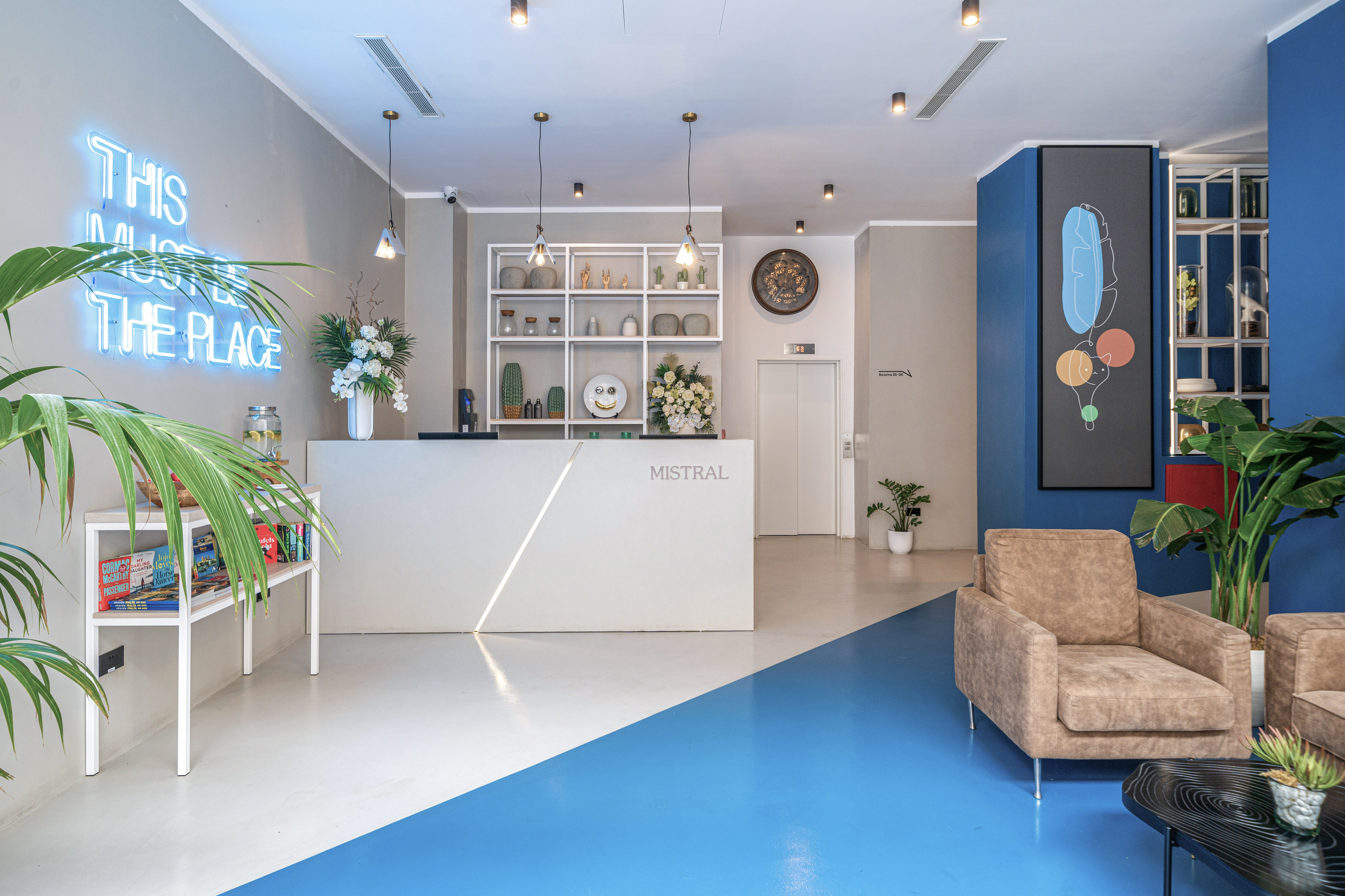 Stylish hotel lobby reception with "MISTRAL" desk, blue neon sign, and vibrant modern decor.