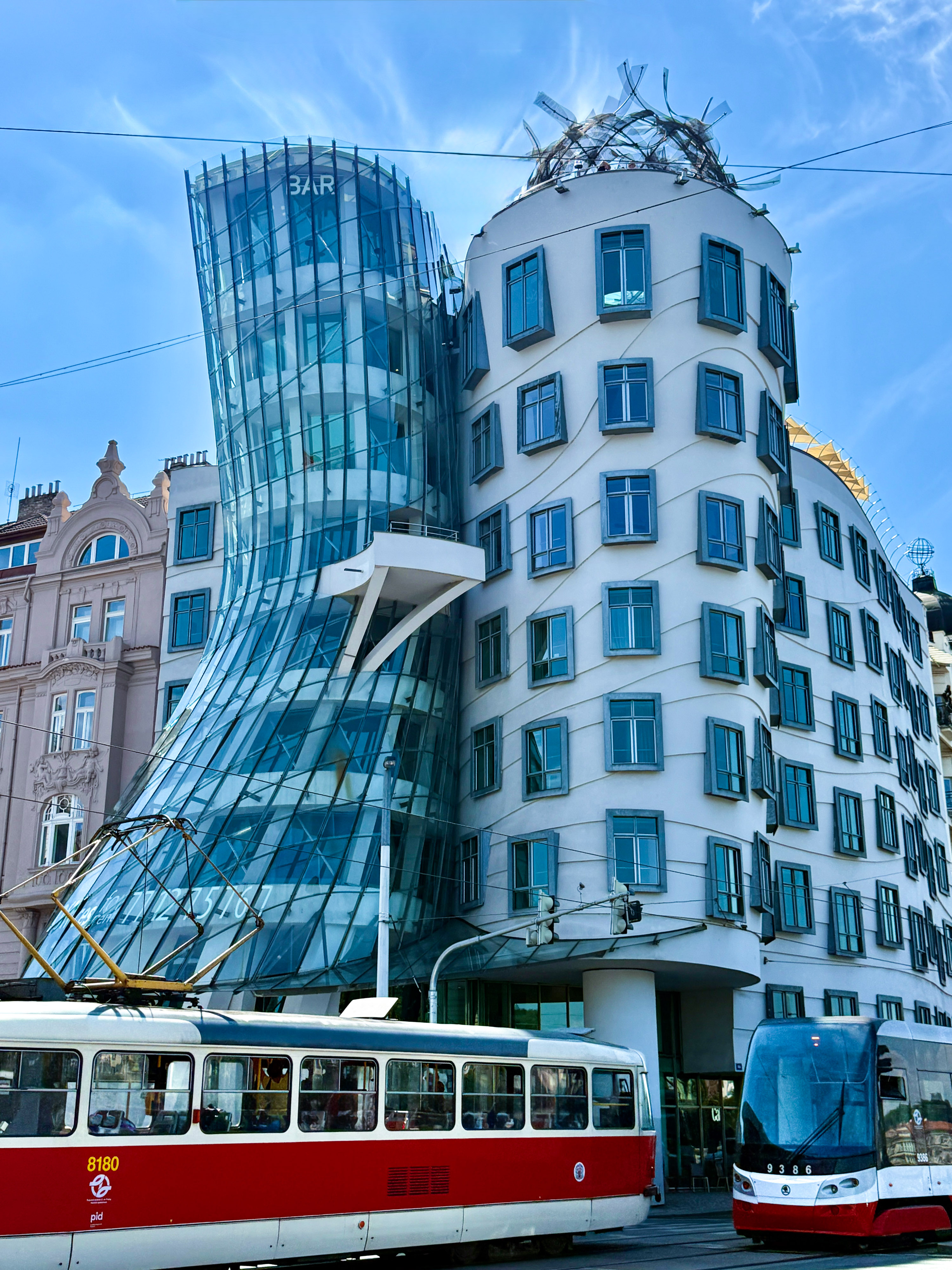 Prague's wavy Dancing House building with glass facades and passing trams.