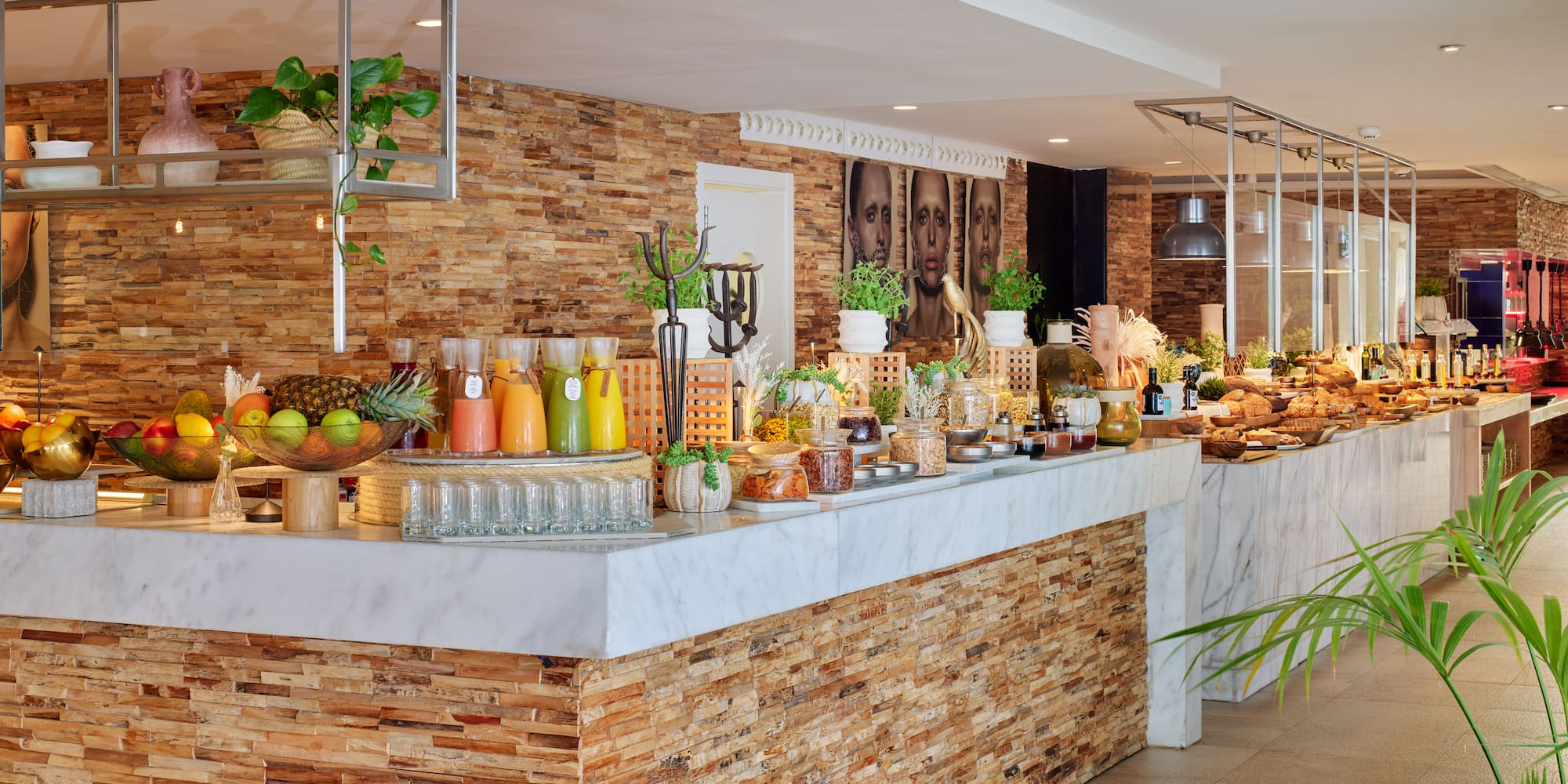 Modern hotel buffet featuring fresh juices, fruits, pastries, and stone wall.