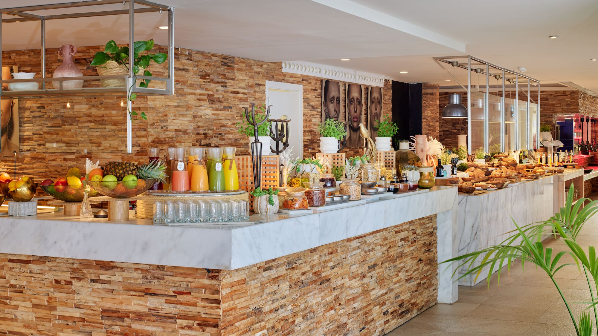 Modern hotel buffet featuring fresh juices, fruits, pastries, and stone wall.