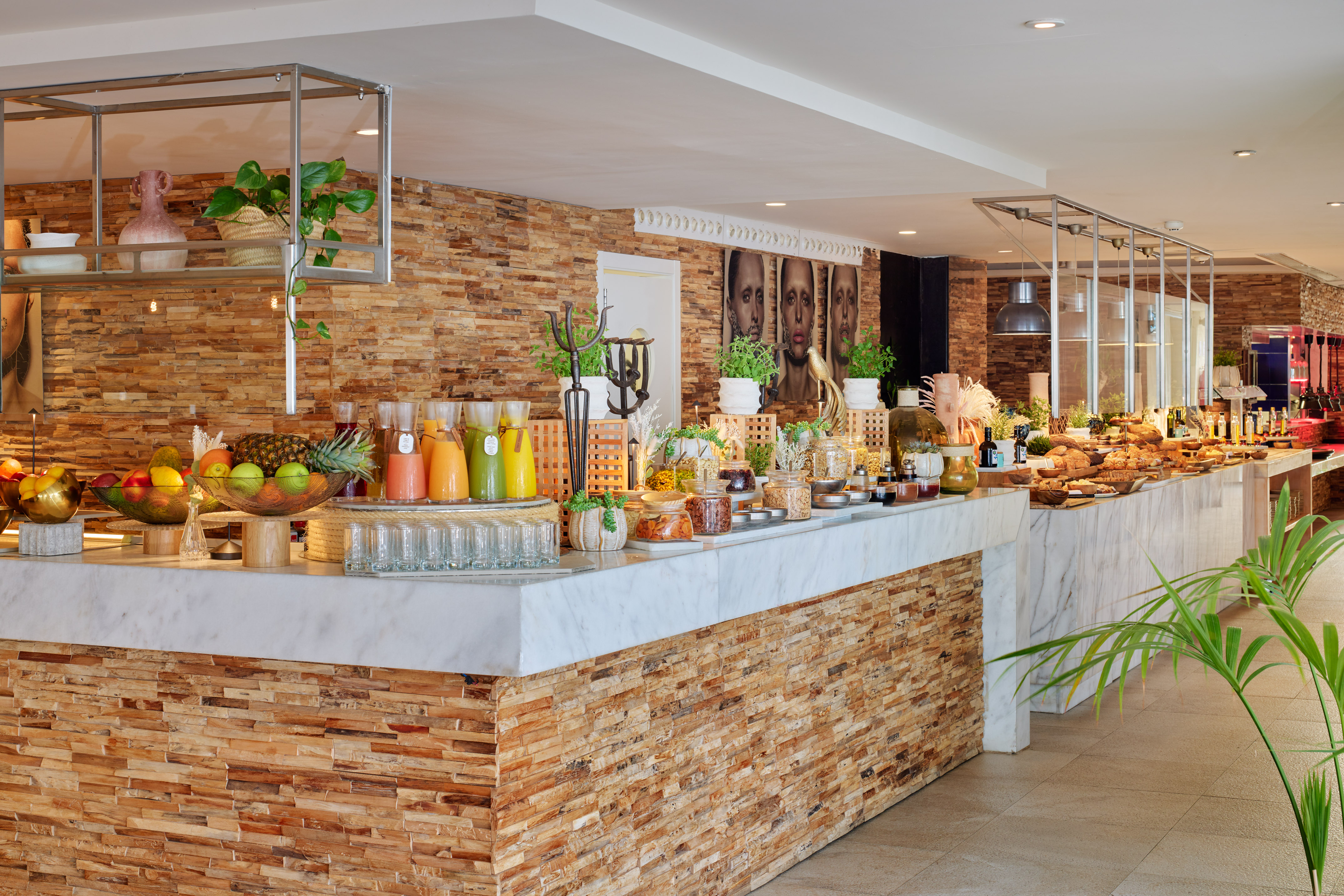 Modern hotel buffet featuring fresh juices, fruits, pastries, and stone wall.