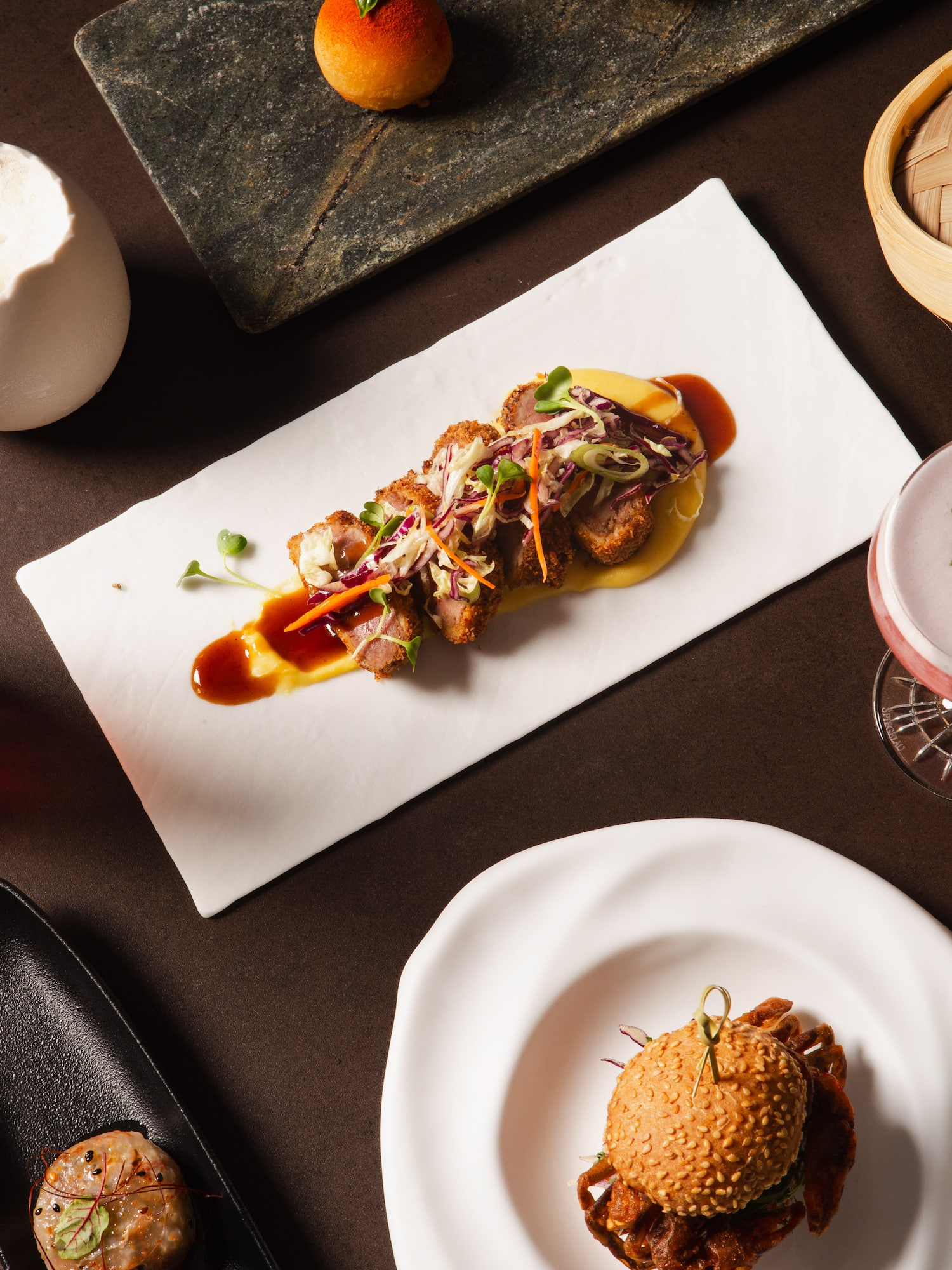 Sliced crispy meat with slaw, soft-shell crab slider, and orange pastry.