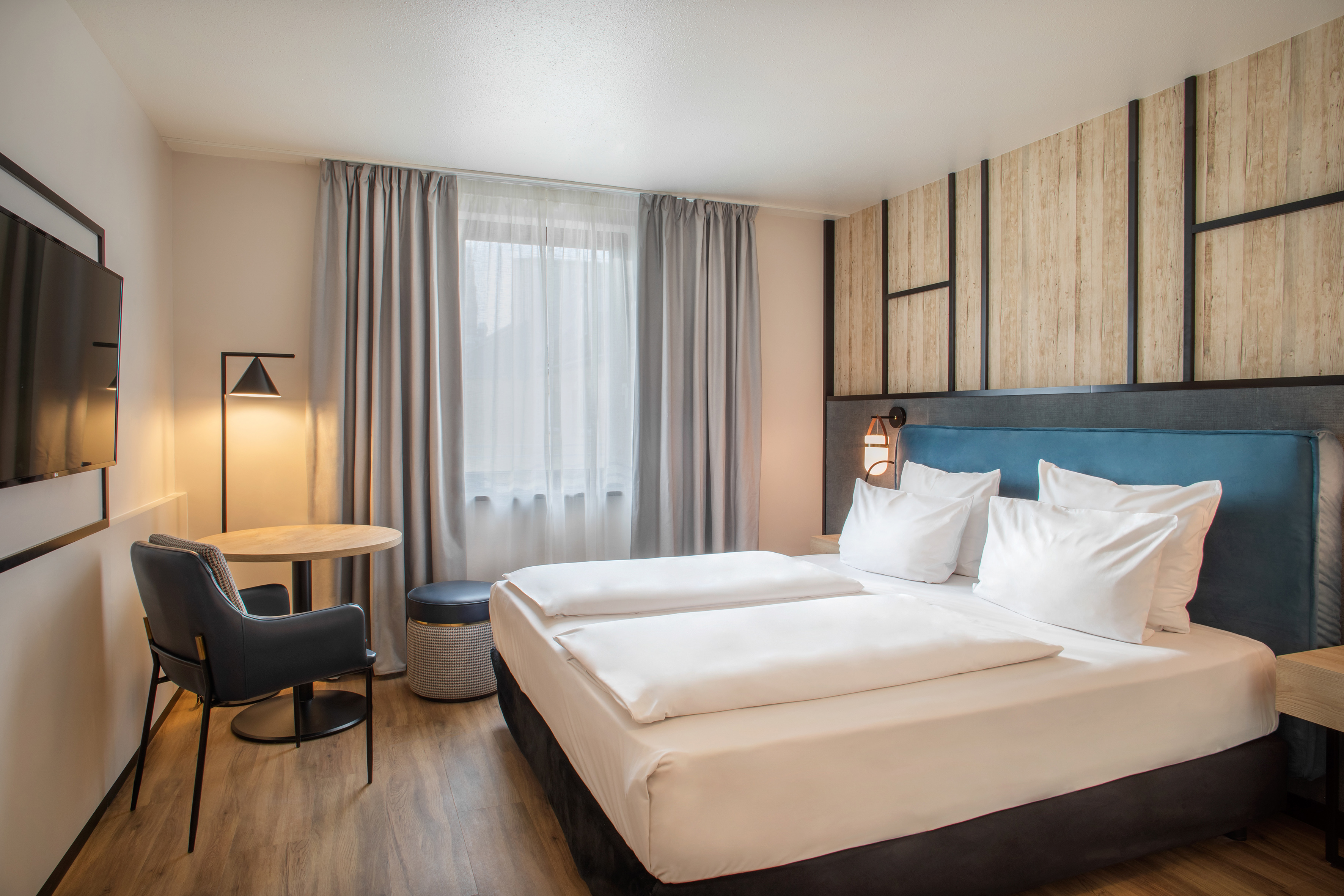 Modern hotel bedroom with bed, blue headboard, wood floor, and seating area.