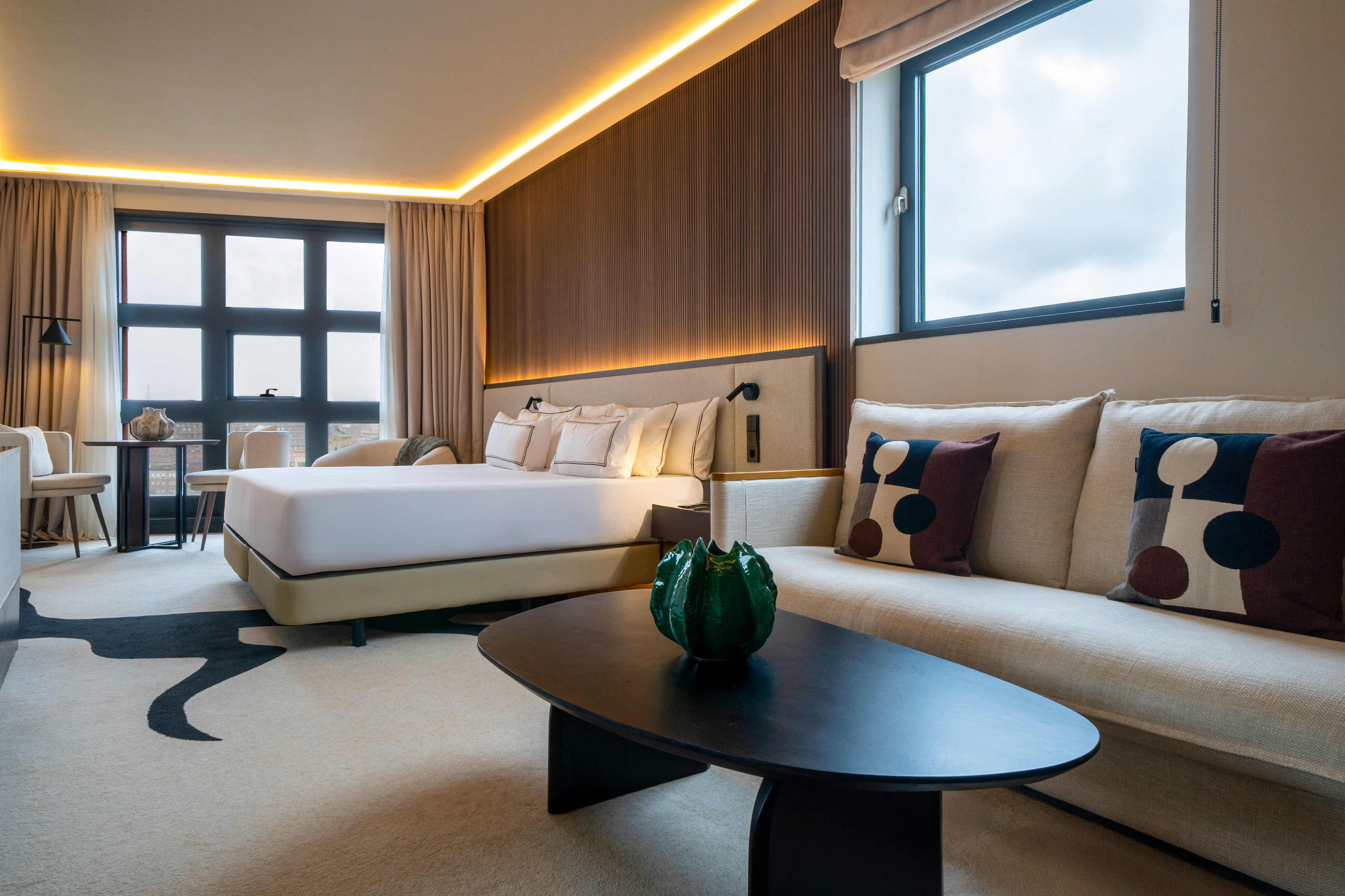 King bed hotel suite with modern sofa, large windows, and ambient lighting.