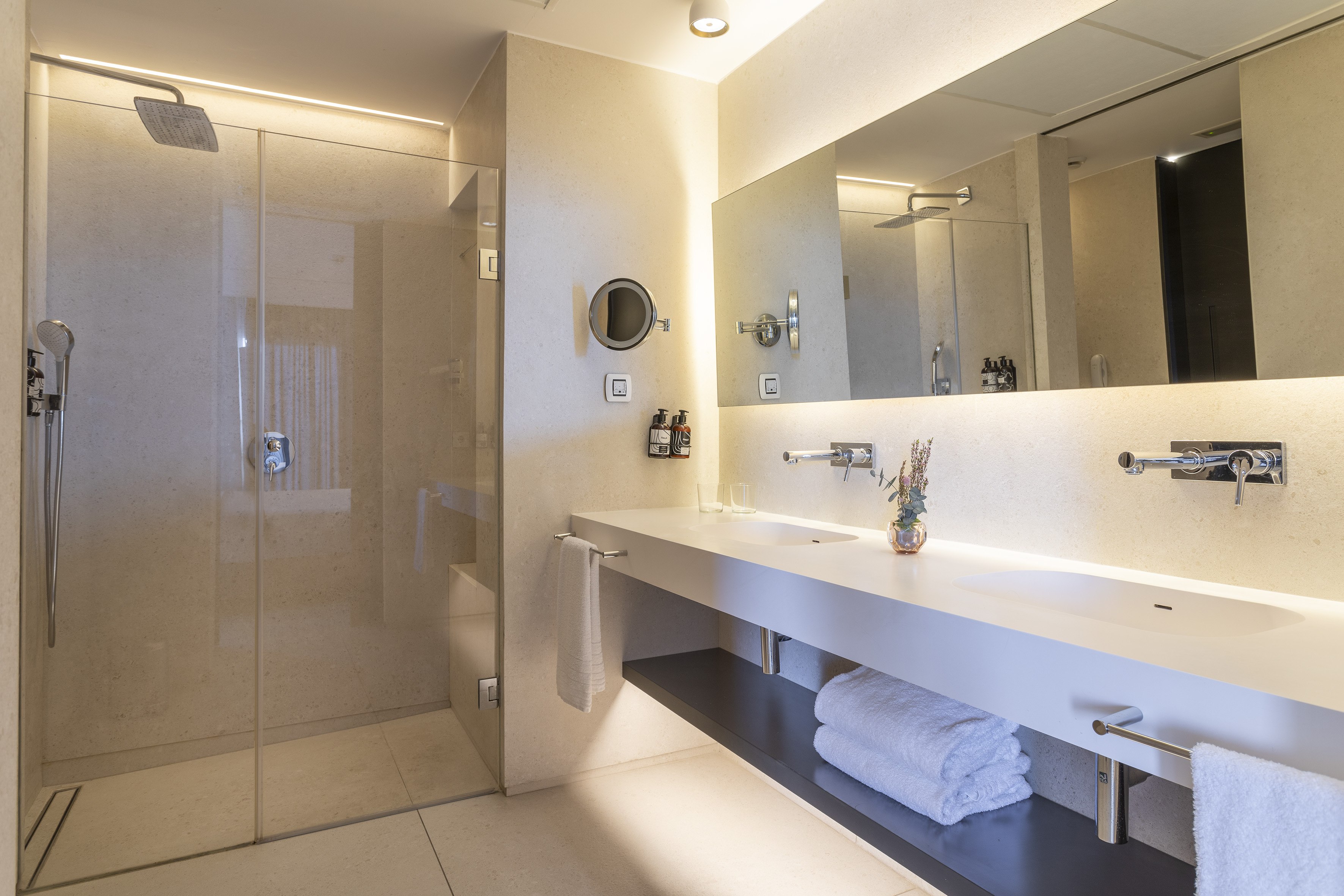 Contemporary bathroom with glass walk-in shower, double vanity, and backlit mirror.