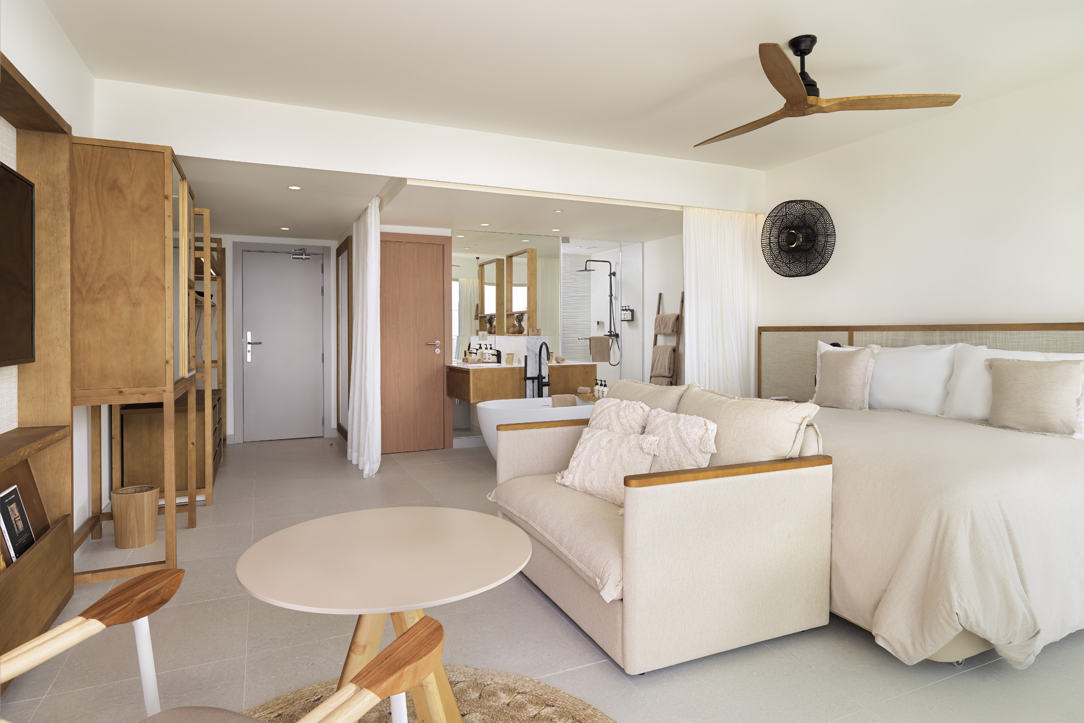 Modern hotel suite with king bed, sofa, natural wood, and integrated bathroom.