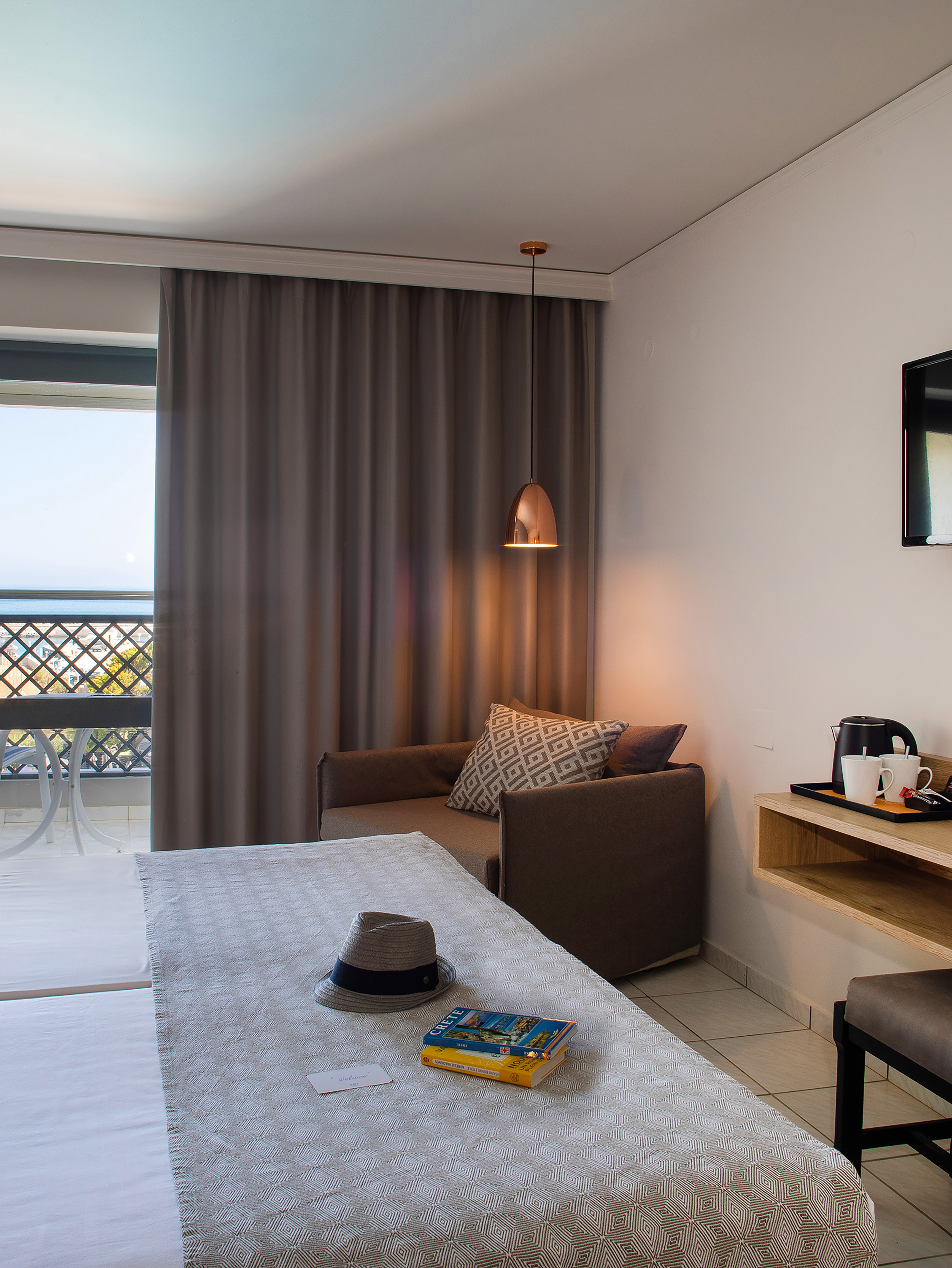 Hotel room with balcony sea view, bed, hat, and Crete travel guides.