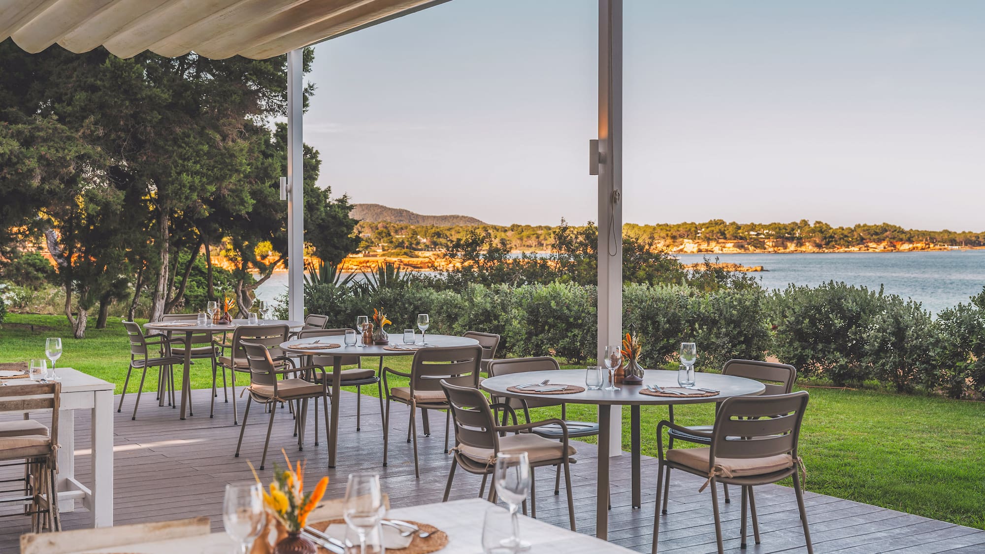 Outdoor dining terrace overlooking the sea, set tables under a shaded canopy.