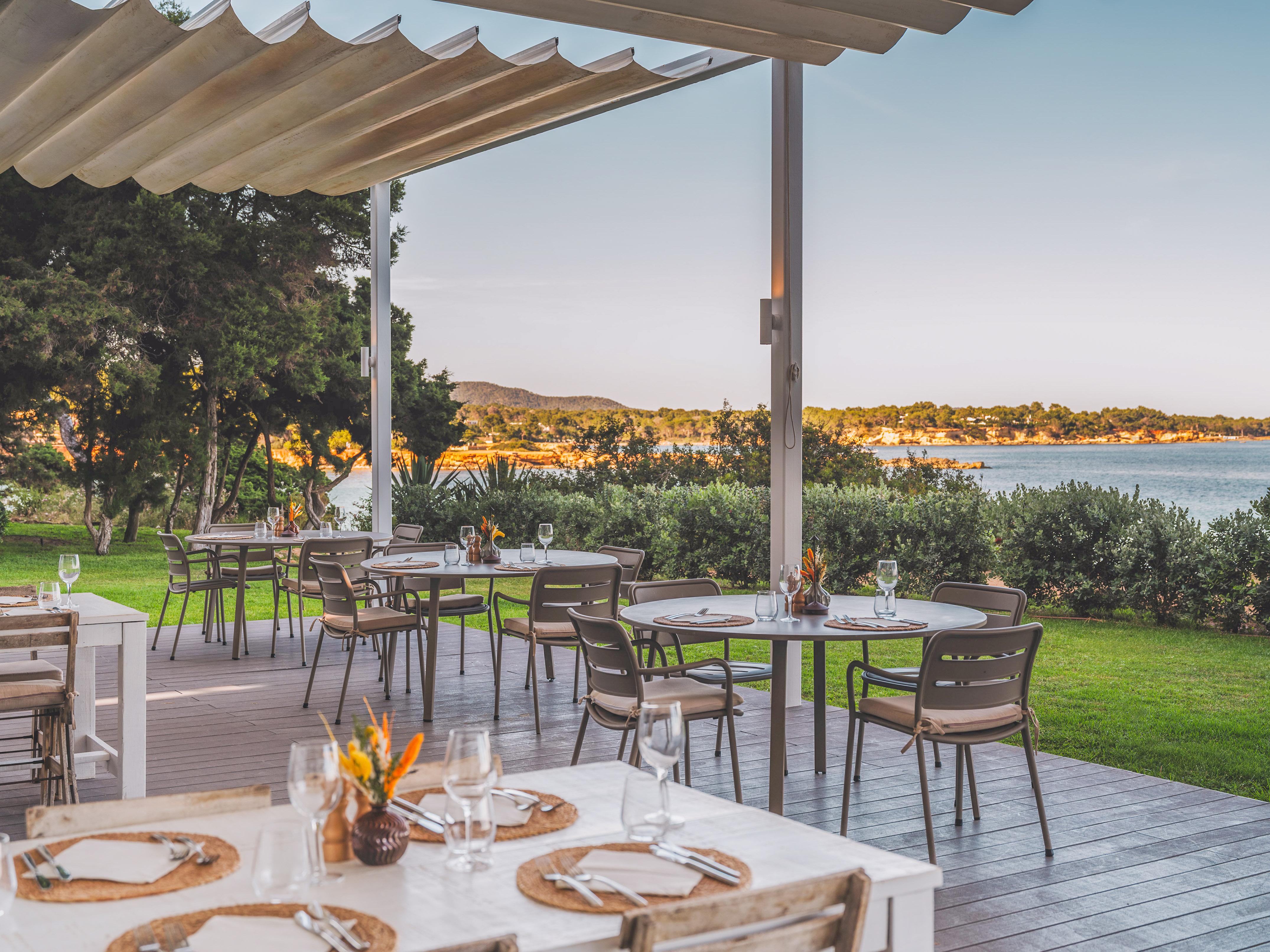 Outdoor dining terrace overlooking the sea, set tables under a shaded canopy.
