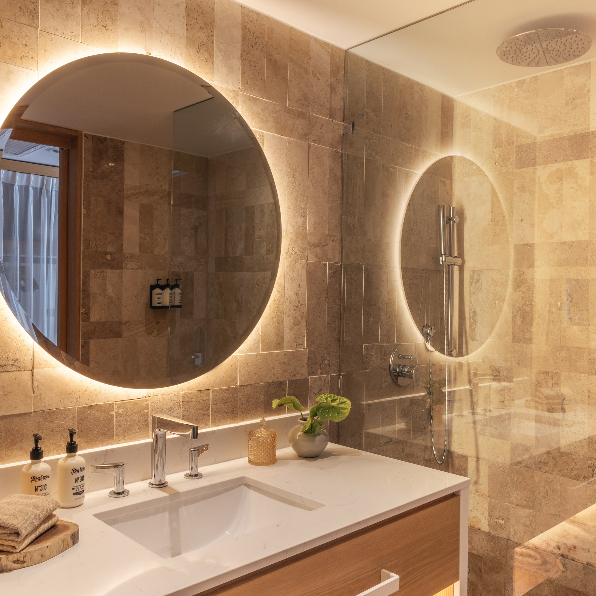 Modern bathroom with backlit mirror, white vanity, and stone-tiled shower.