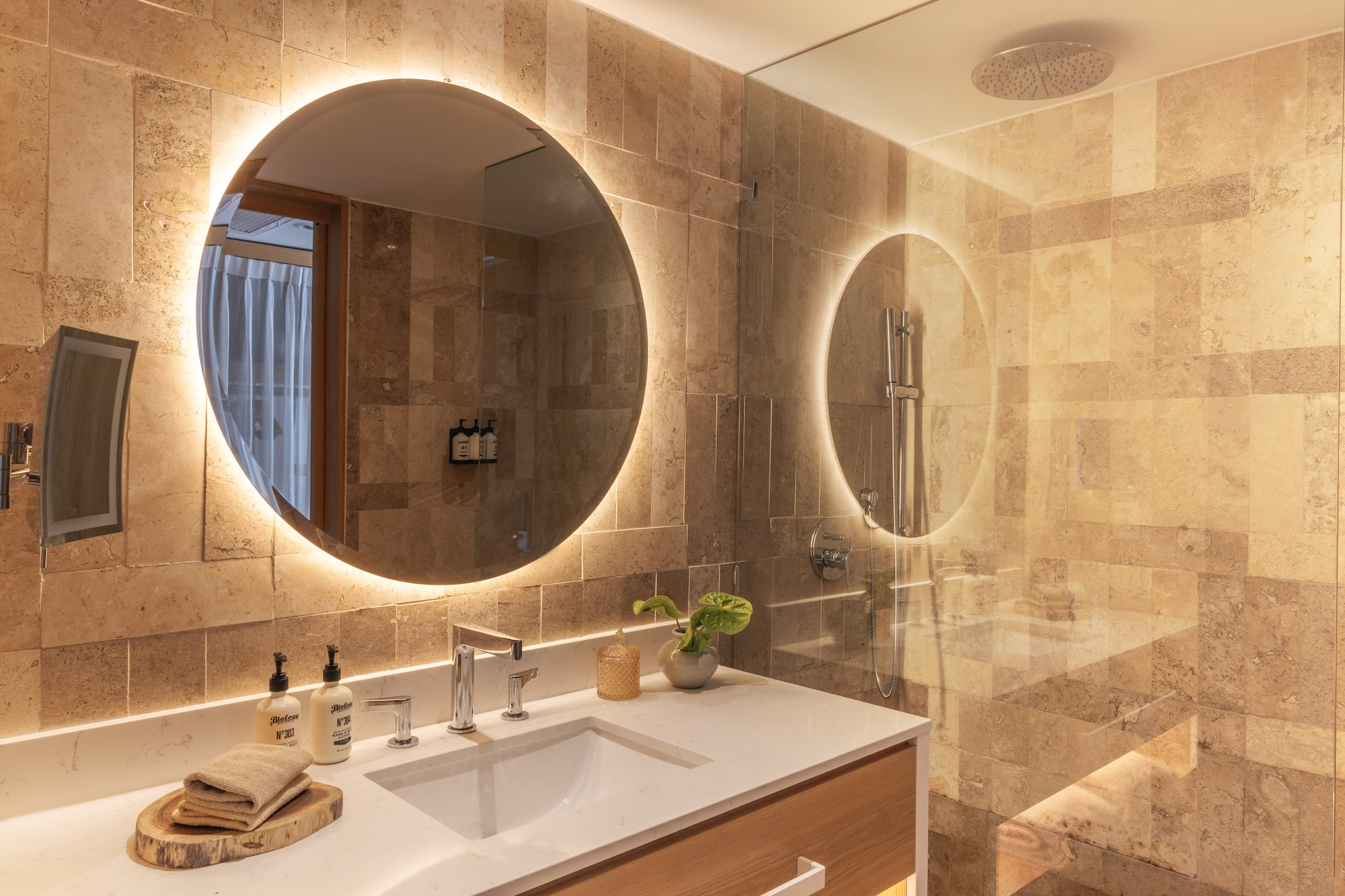 Modern bathroom with backlit mirror, white vanity, and stone-tiled shower.