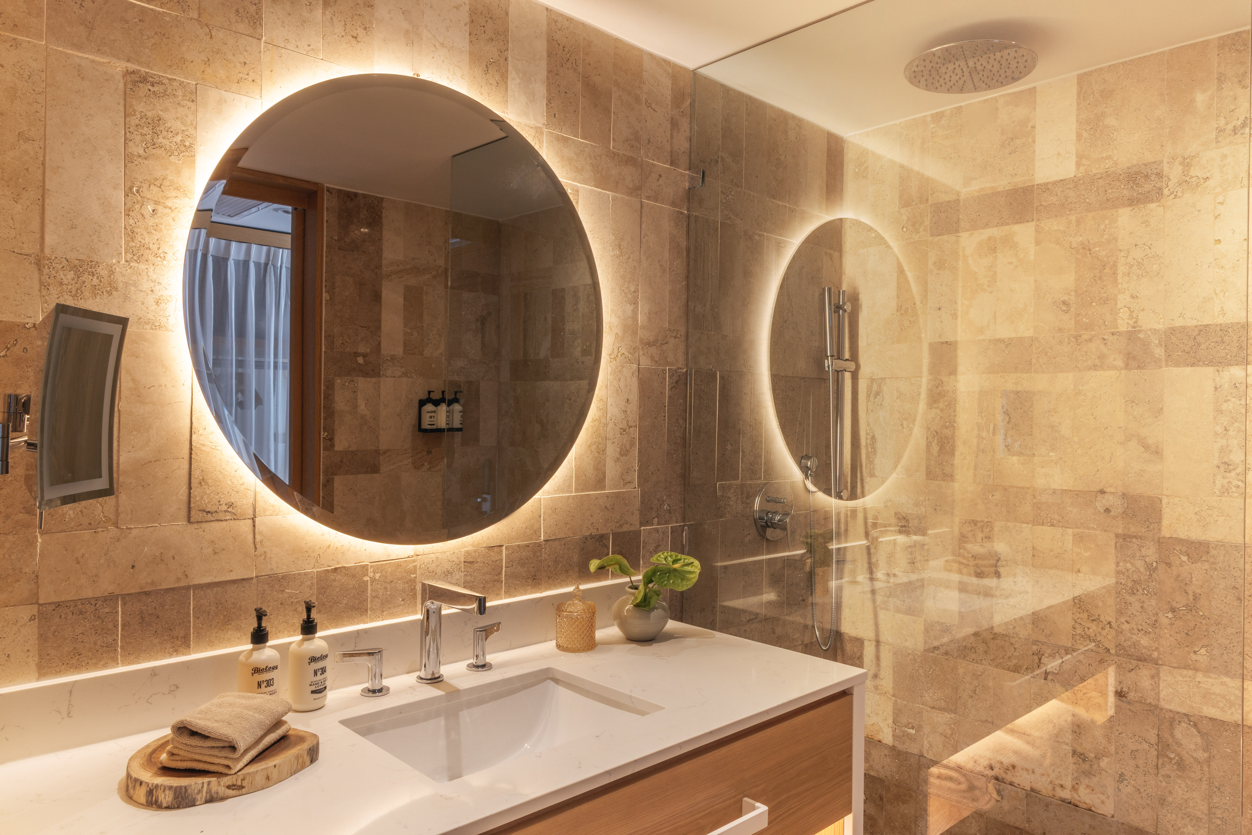 Modern bathroom with backlit mirror, white vanity, and stone-tiled shower.
