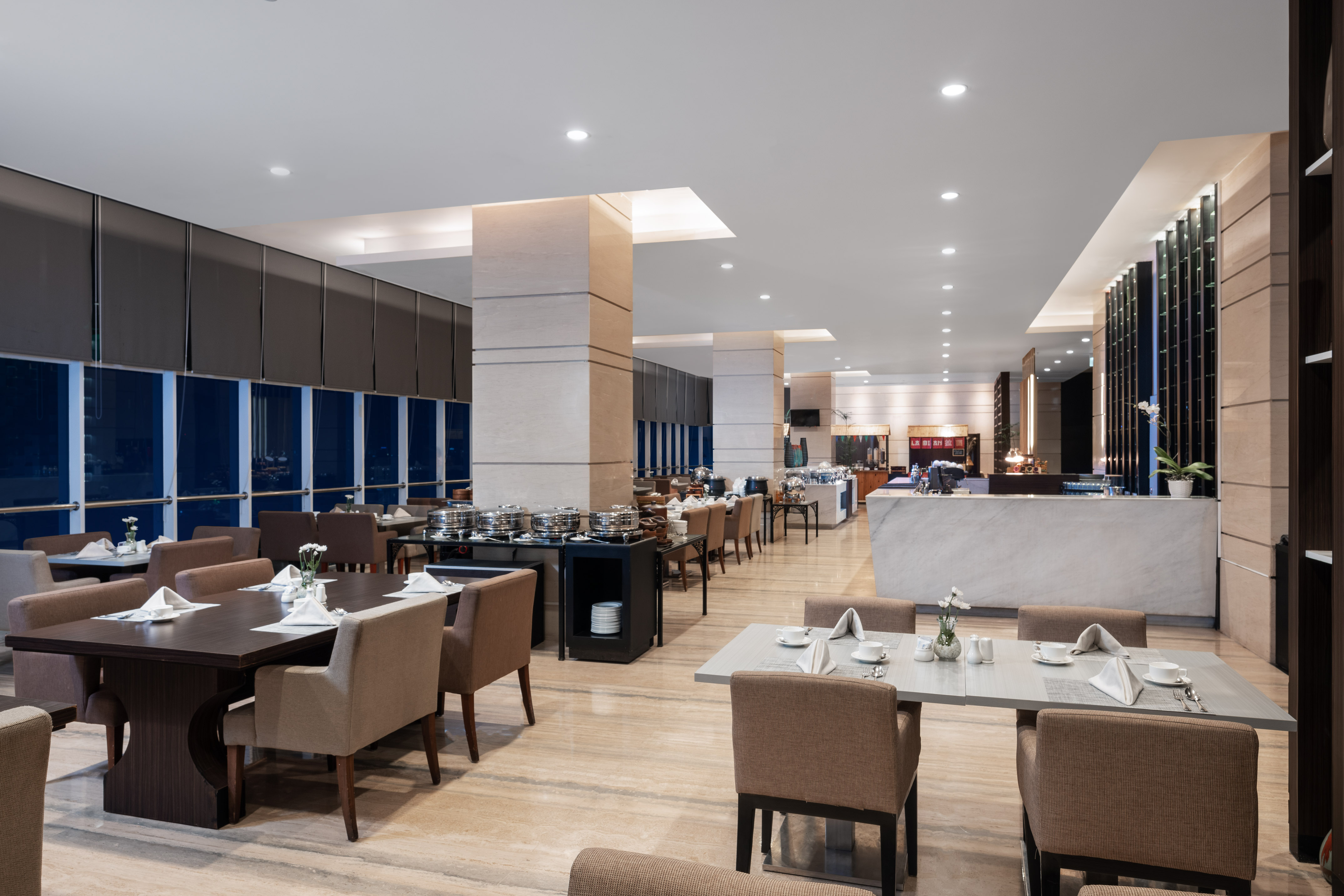 Modern hotel restaurant dining area with buffet setup and set tables.