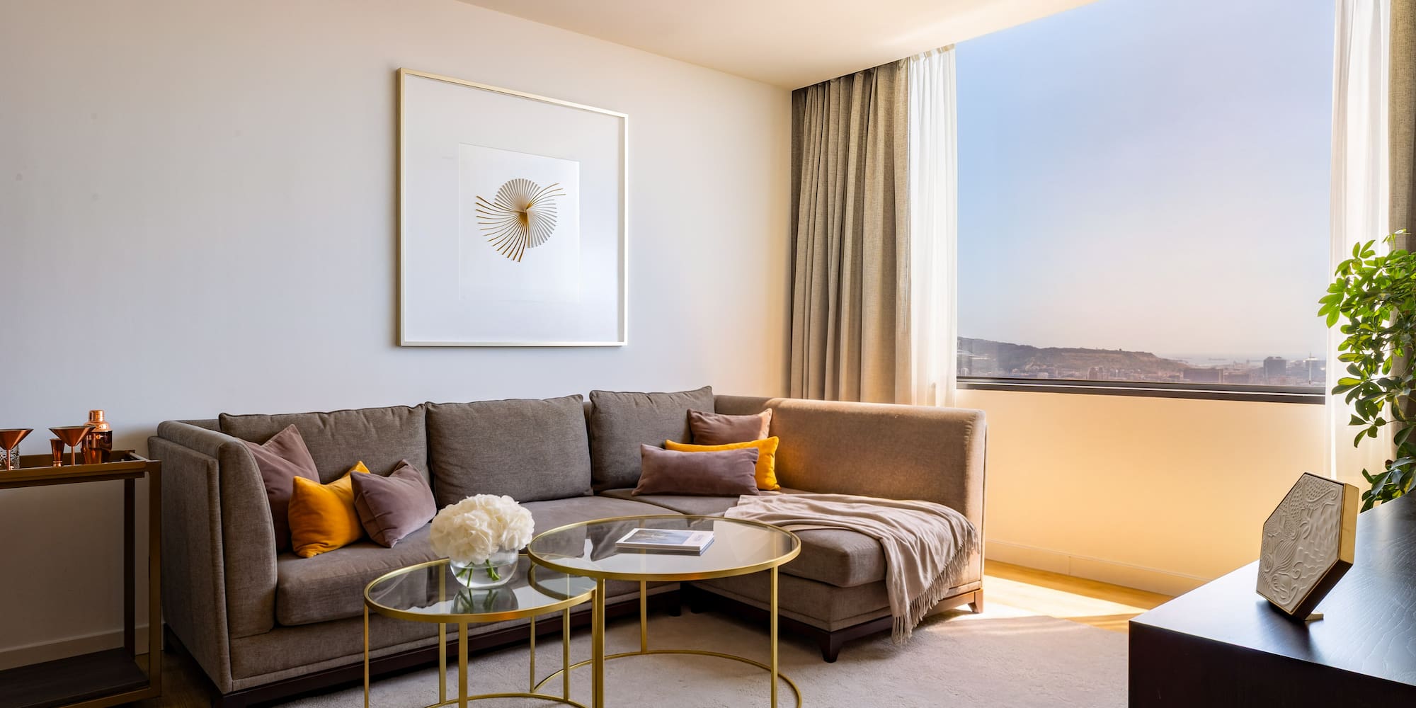 Stylish living room with brown sectional, modern art, and sunny window city view.