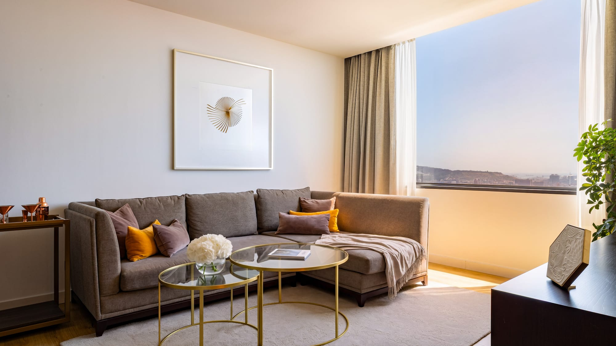 Stylish living room with brown sectional, modern art, and sunny window city view.