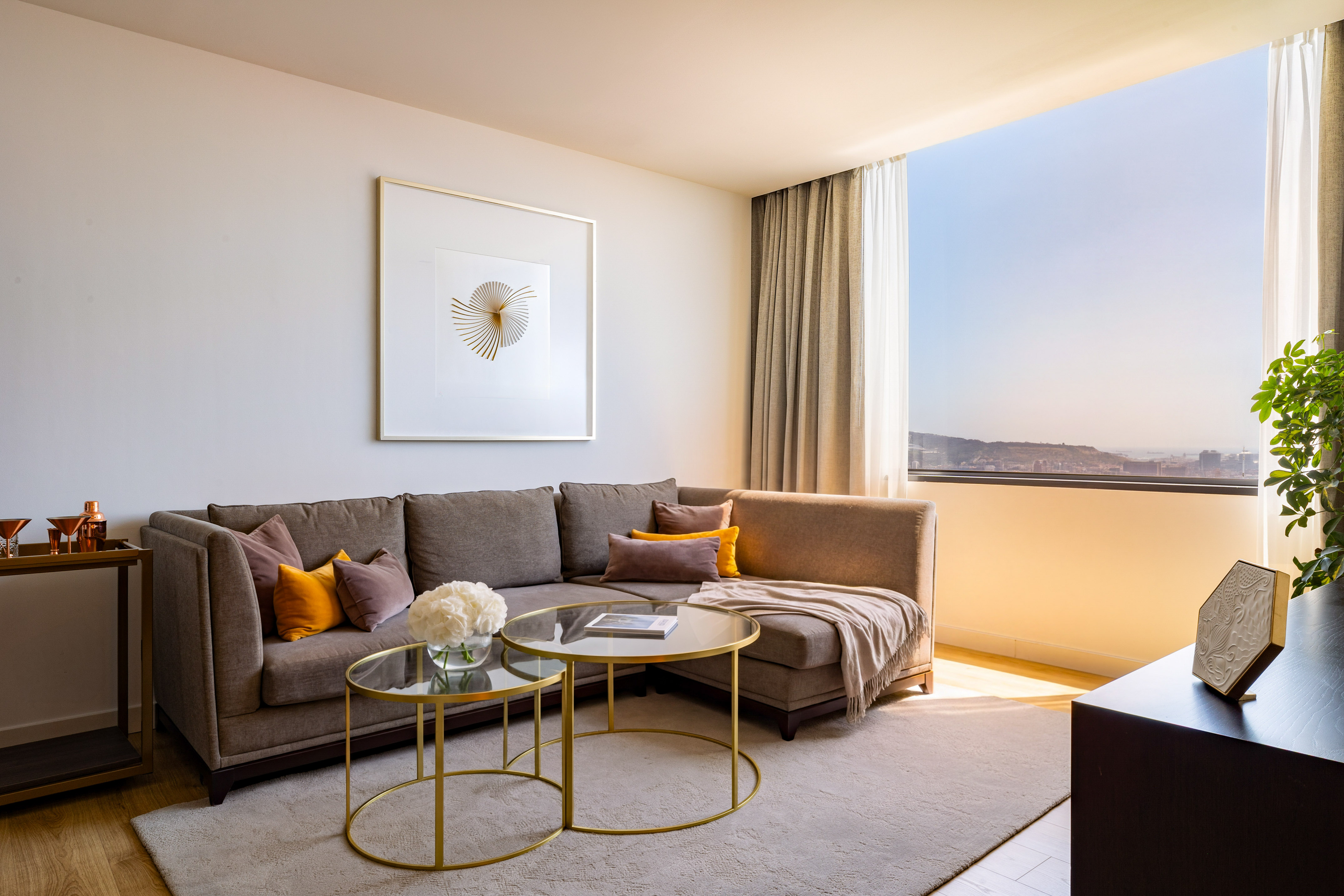 Stylish living room with brown sectional, modern art, and sunny window city view.