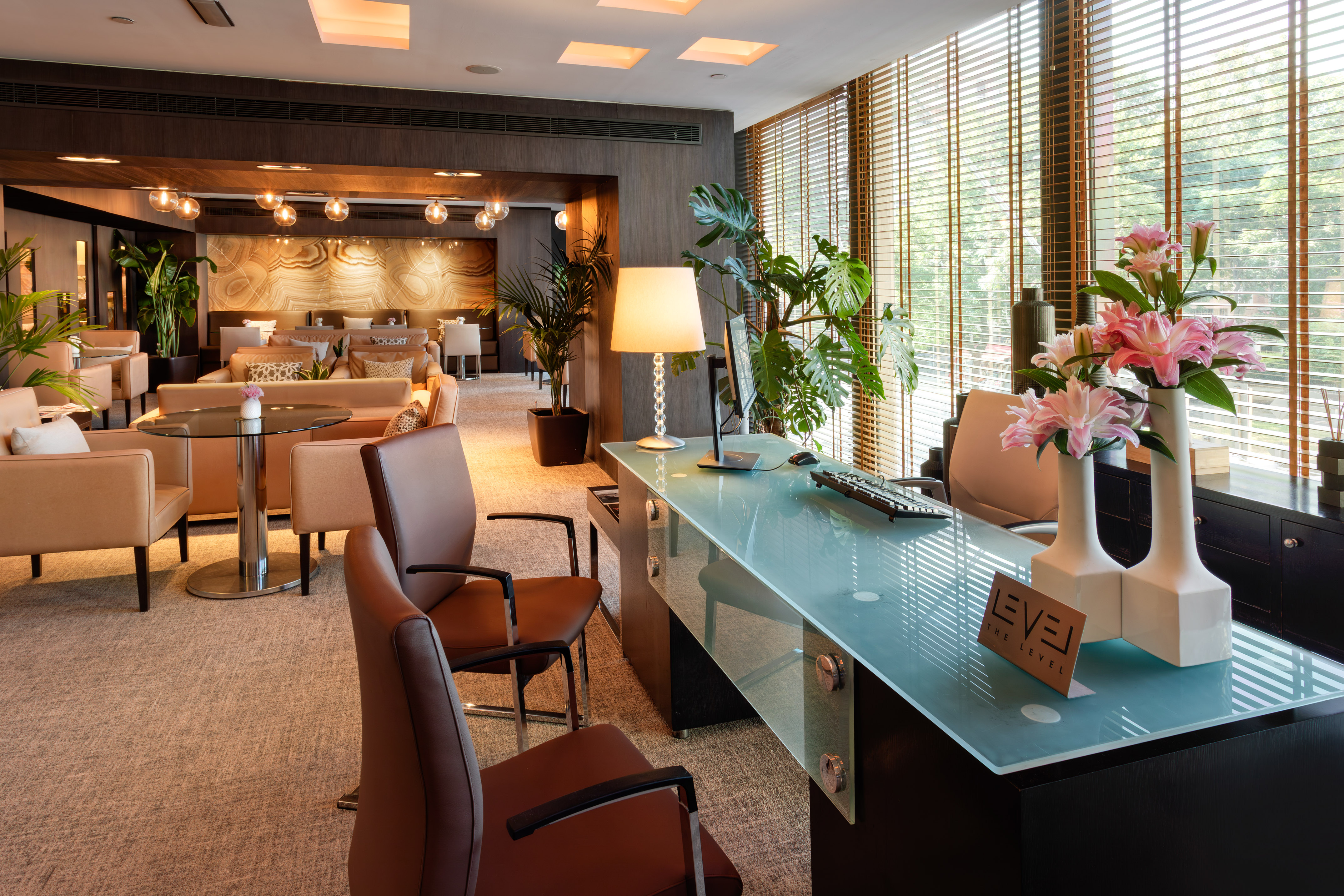 Modern hotel reception with glass desk, brown chairs, and luxurious lounge.
