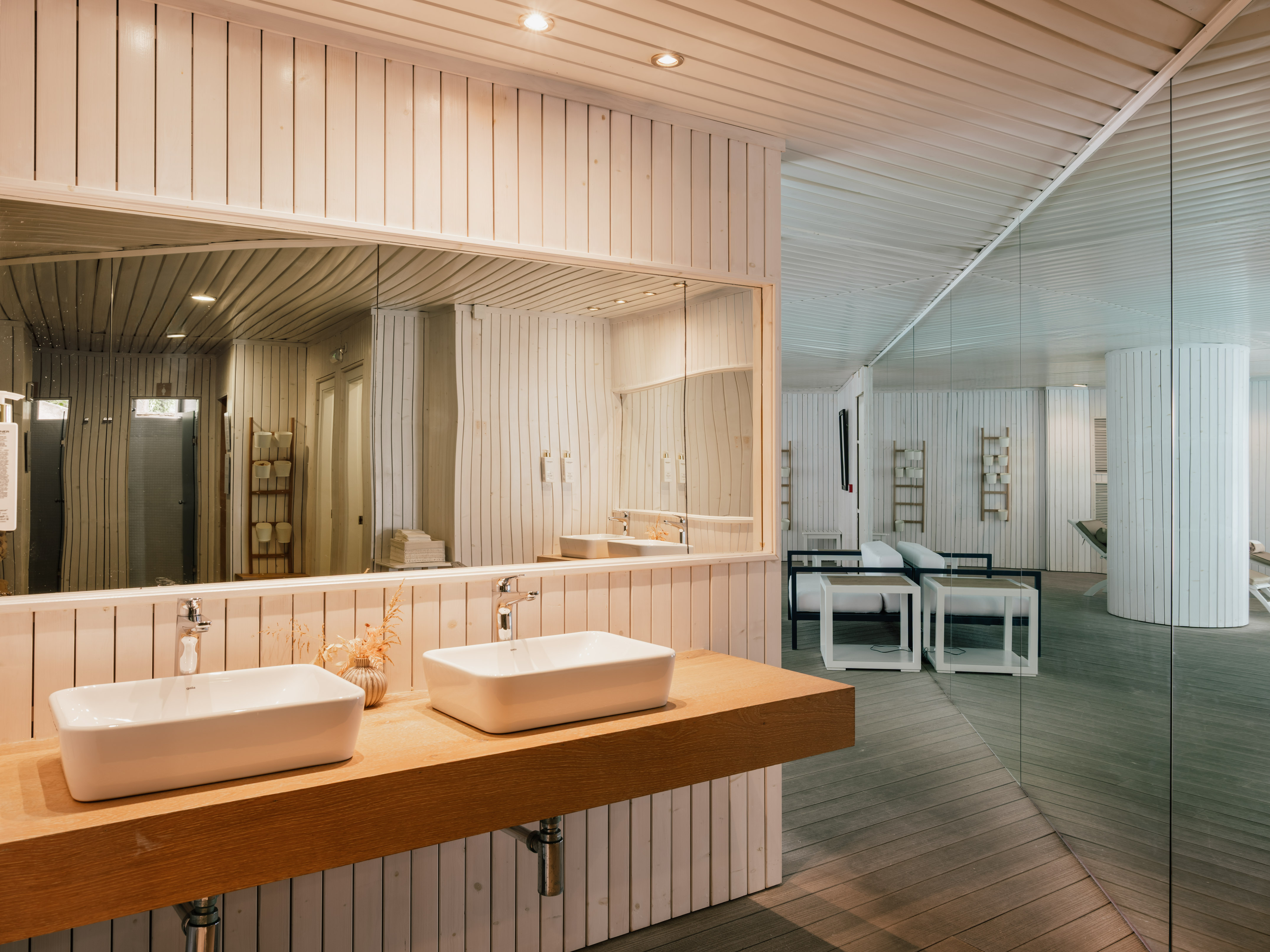 Modern spa bathroom with twin sinks on a wooden counter, white wood paneling.