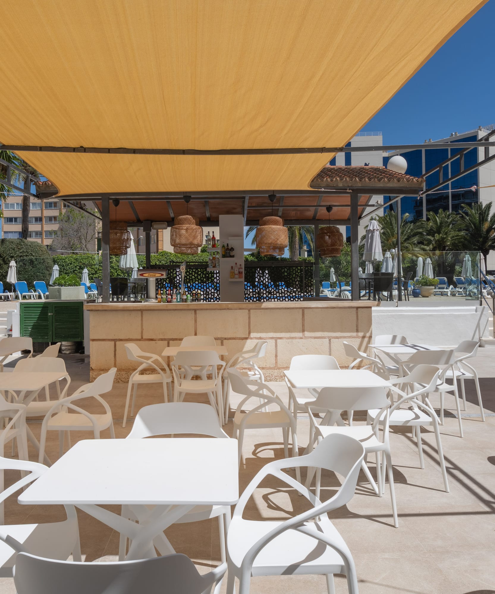 Shaded outdoor hotel pool bar with white seating, yellow canopies.