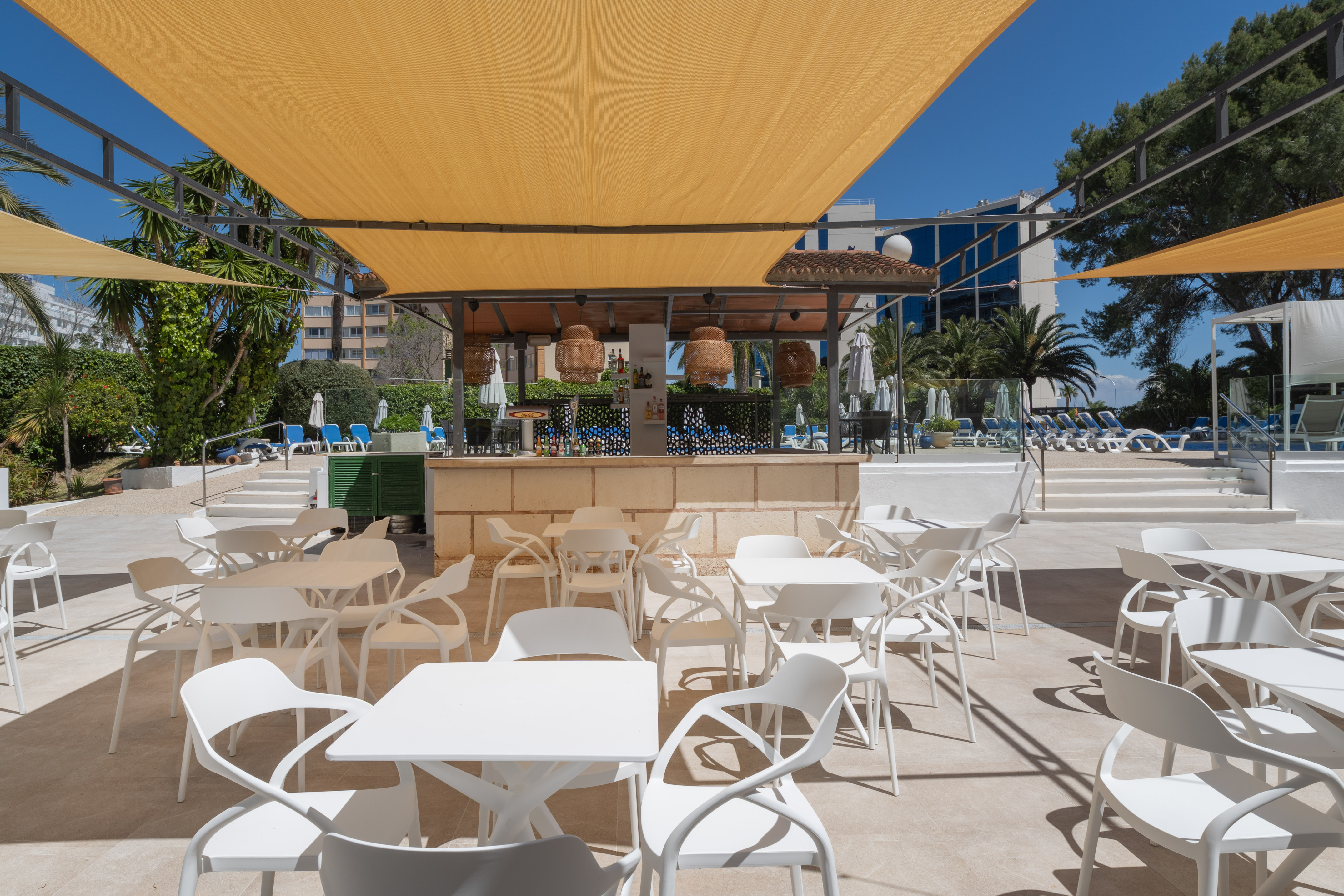 Shaded outdoor hotel pool bar with white seating, yellow canopies.