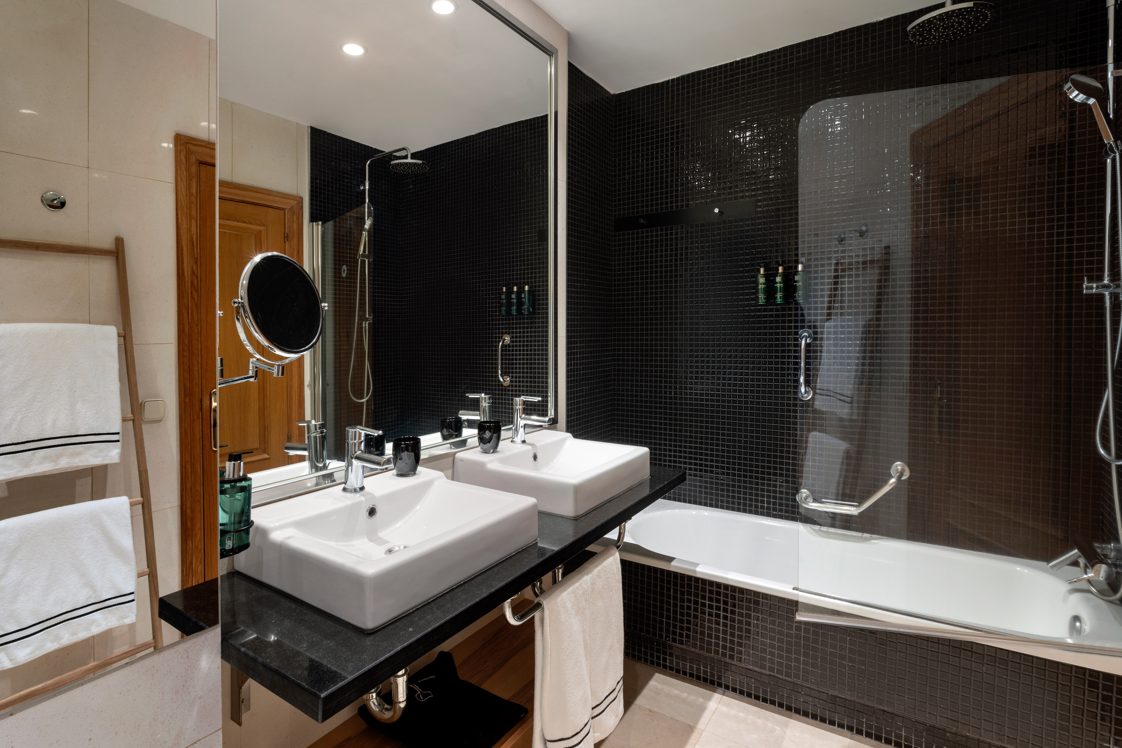 Modern bathroom with black mosaic tiles, double vanity, and bathtub with shower.