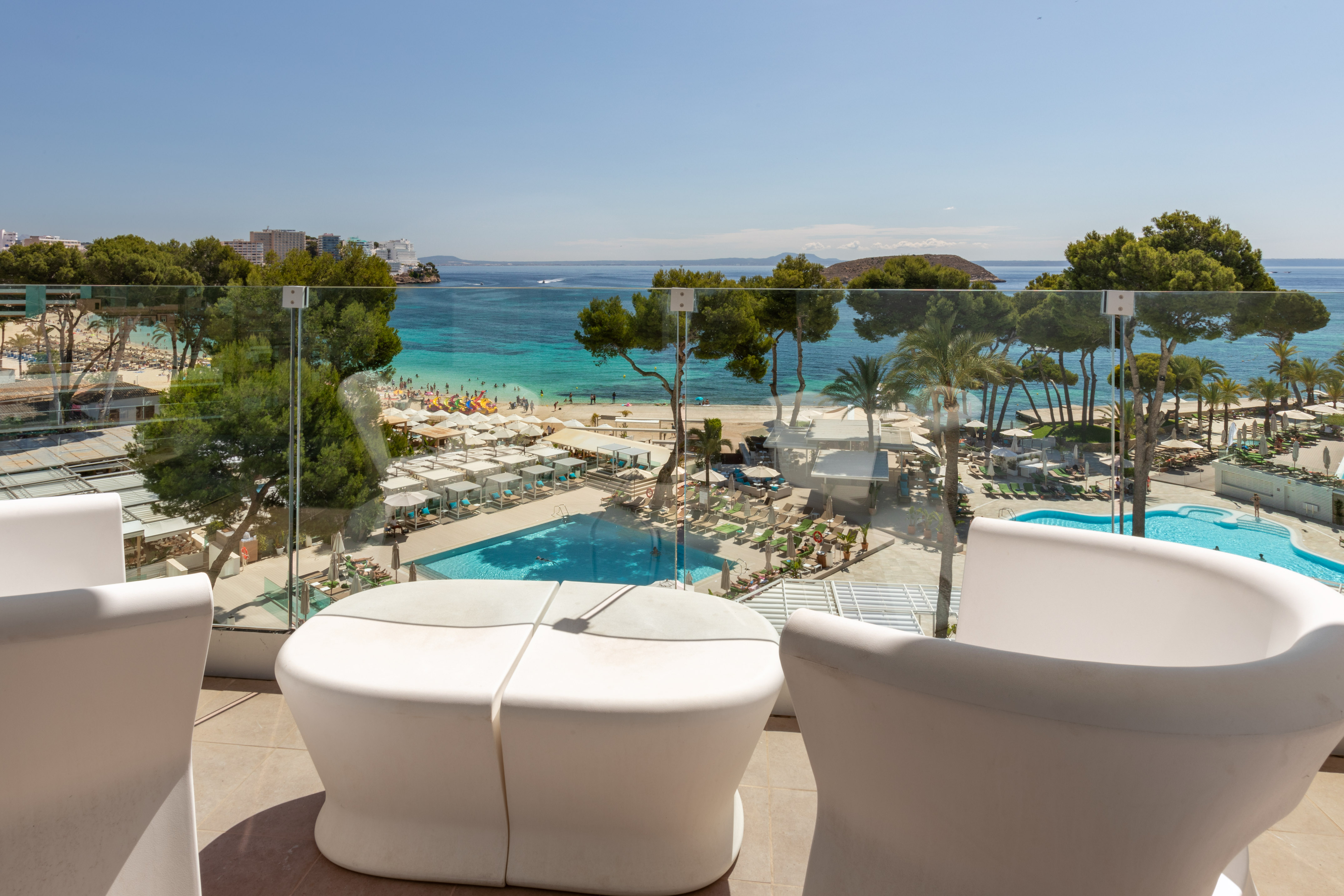 Balcony view of sunny beach resort with turquoise sea and swimming pool.