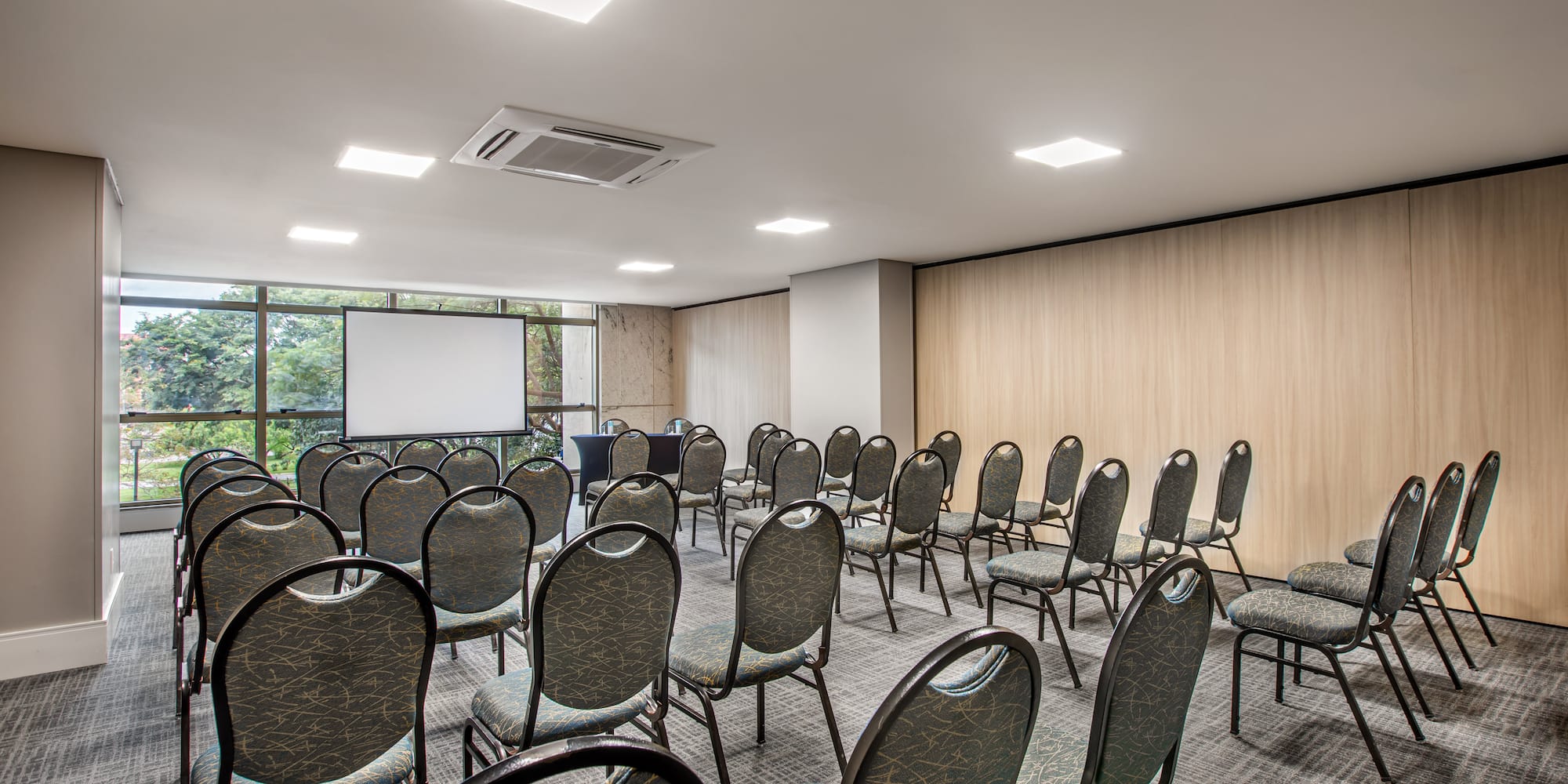 Modern meeting room with rows of chairs, projector screen, and wooden walls.
