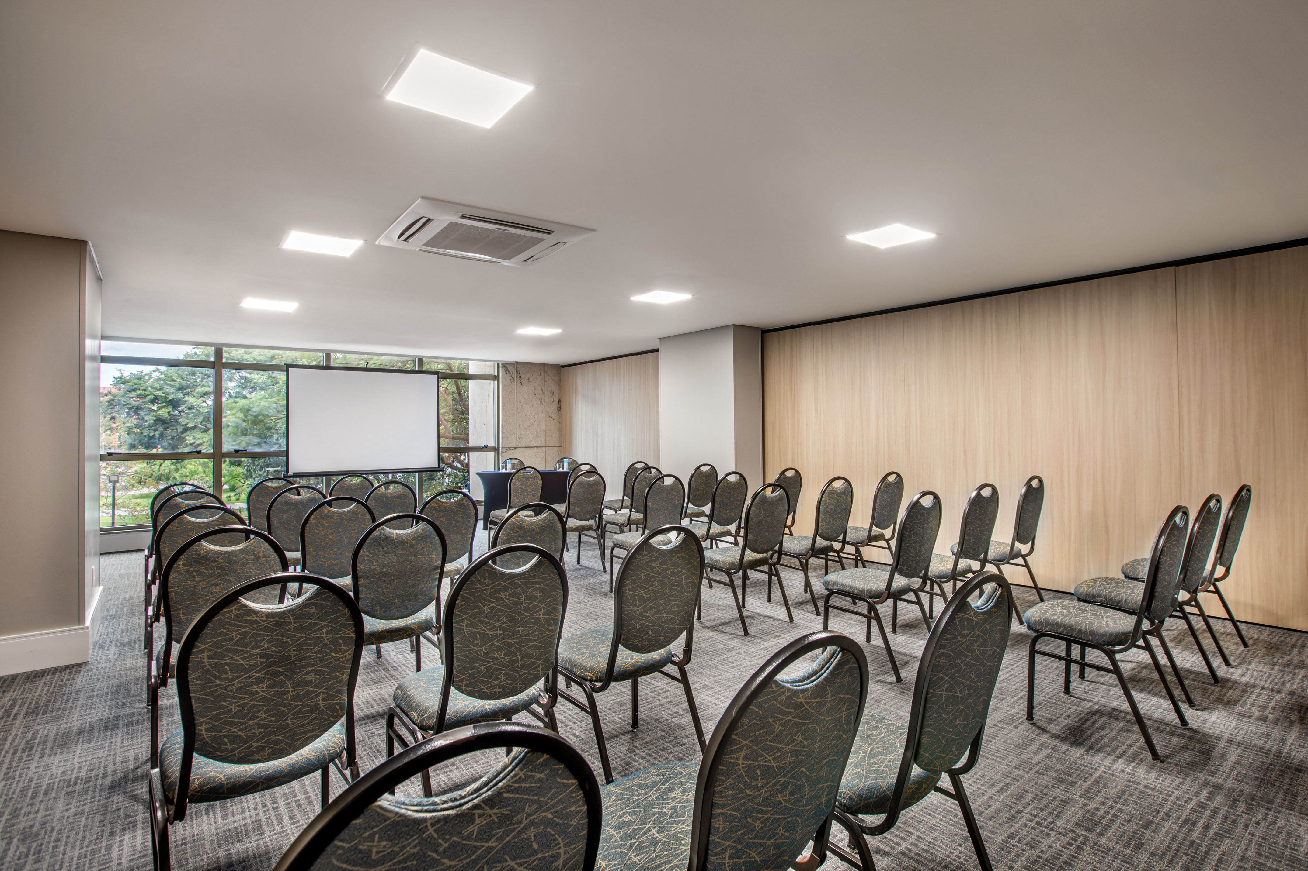 Modern meeting room with rows of chairs, projector screen, and wooden walls.