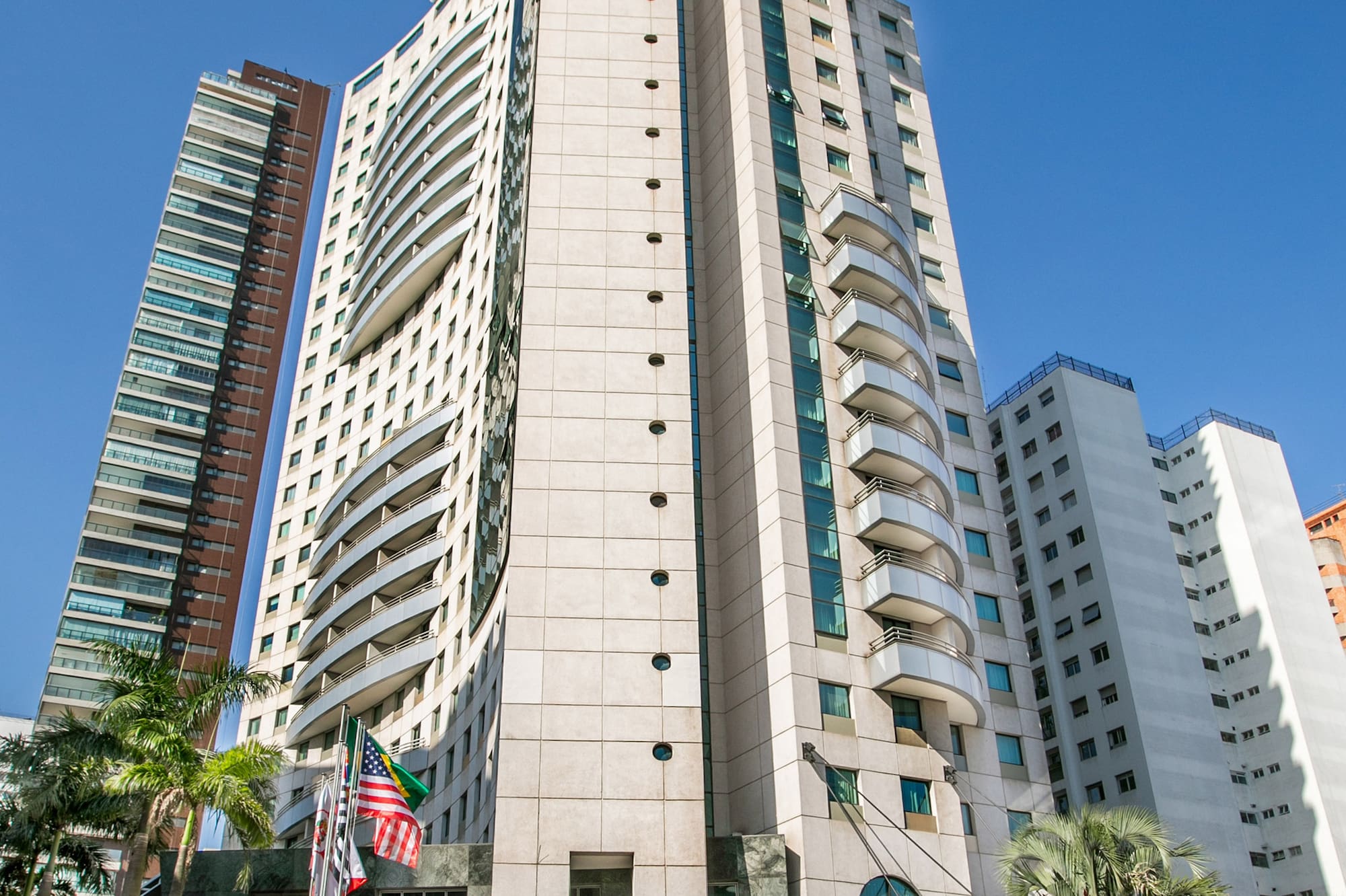 Tall Melia hotel building and modern skyscrapers under blue sky with palm trees.