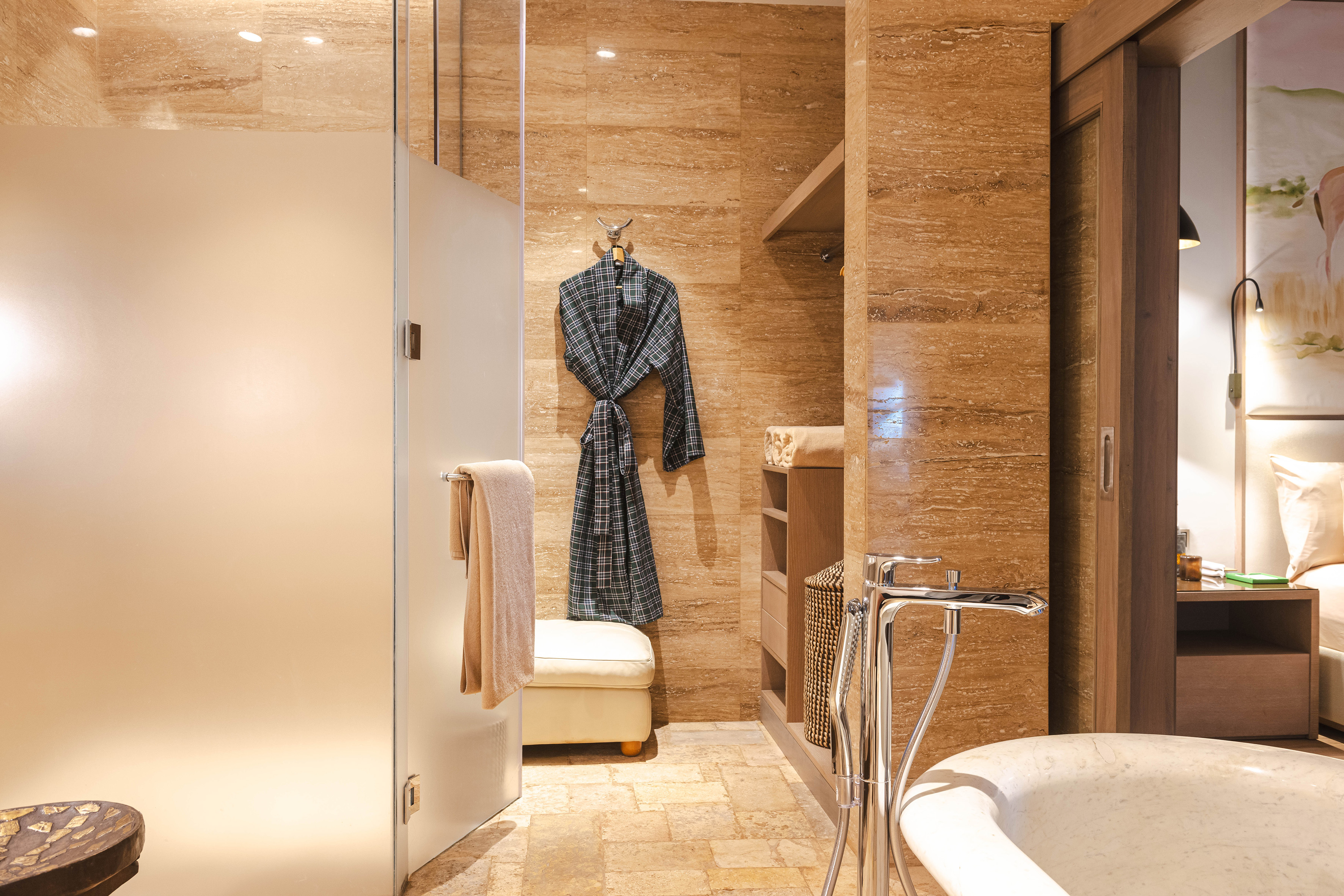 Elegant travertine bathroom with frosted glass shower and freestanding tub.