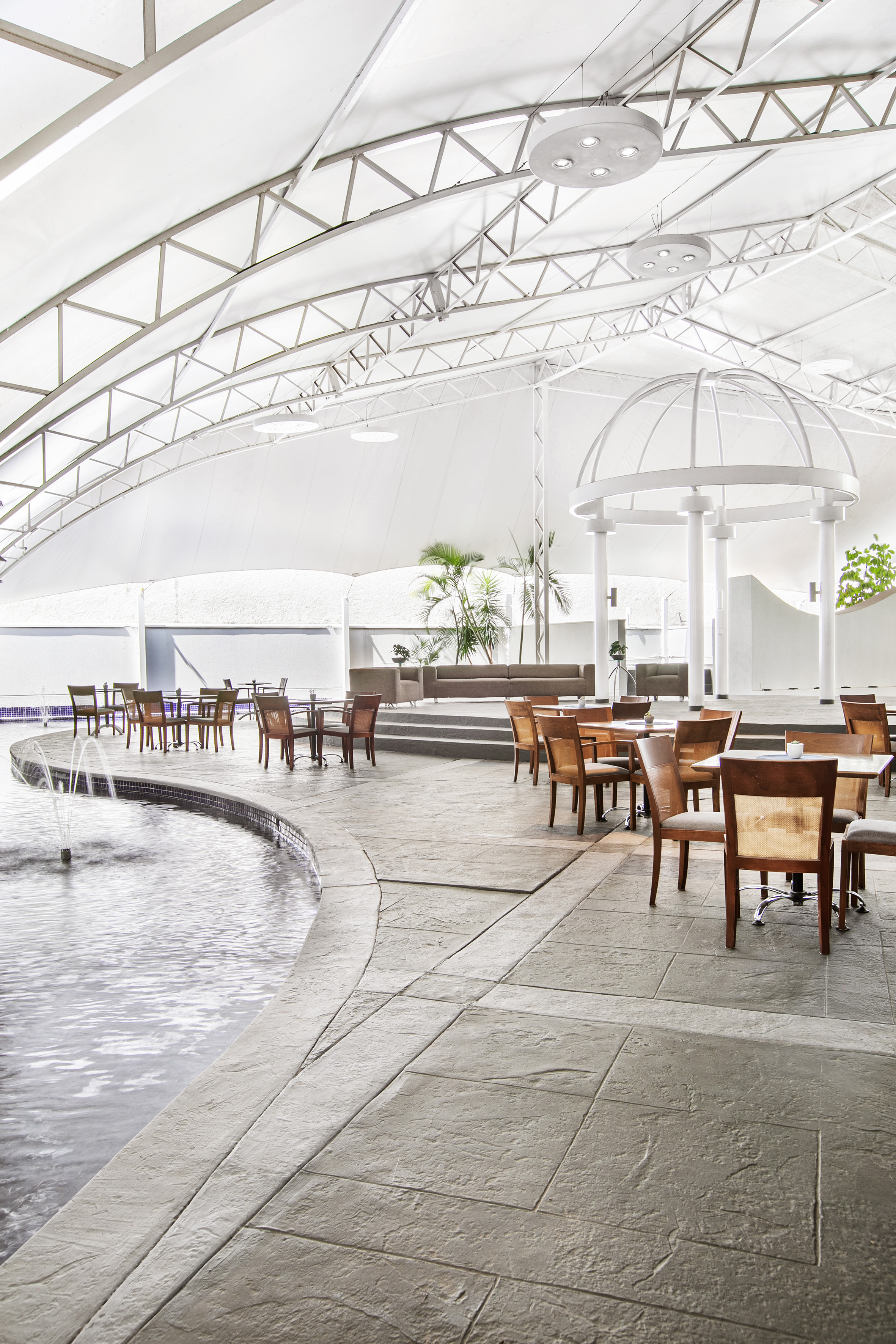 Resort poolside lounge with white tensile roof, fountain, dining, and gazebo.