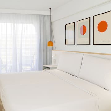 a bed with white sheets and orange art on the wall