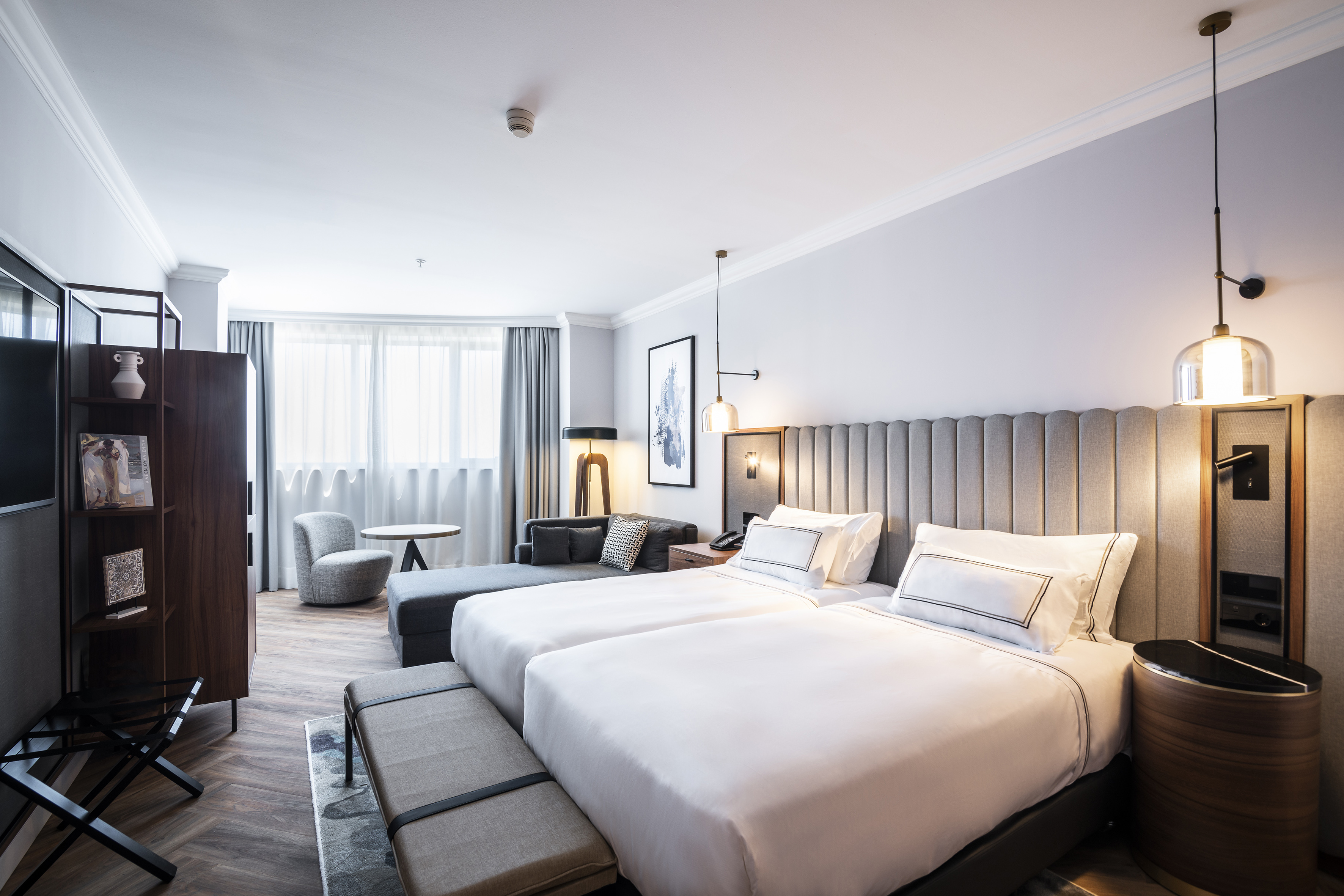 Habitación doble de hotel moderna con dos camas, sofá y ventanal luminoso.