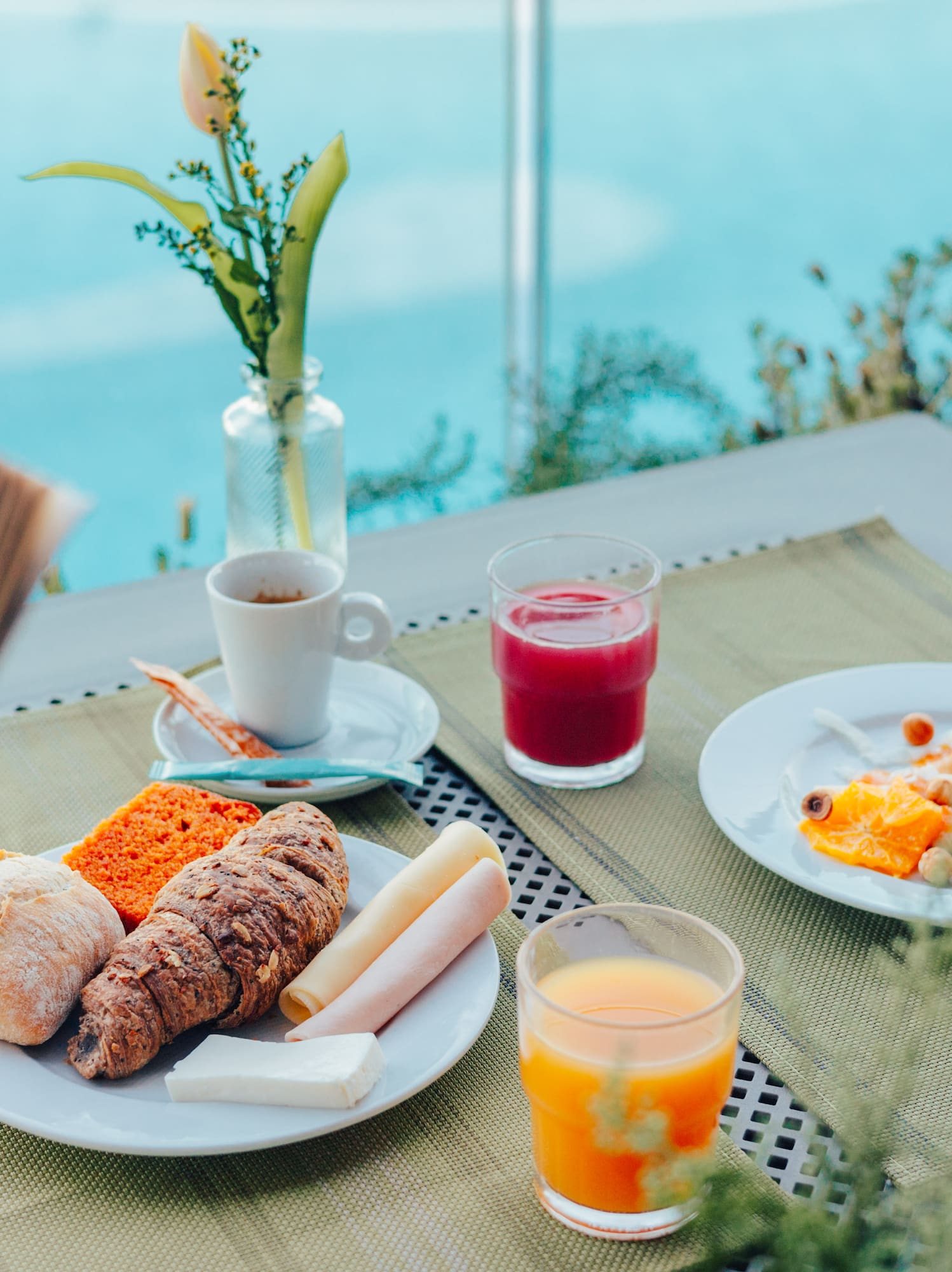 Outdoor breakfast by pool: pastries, coffee, juices, and person reading.