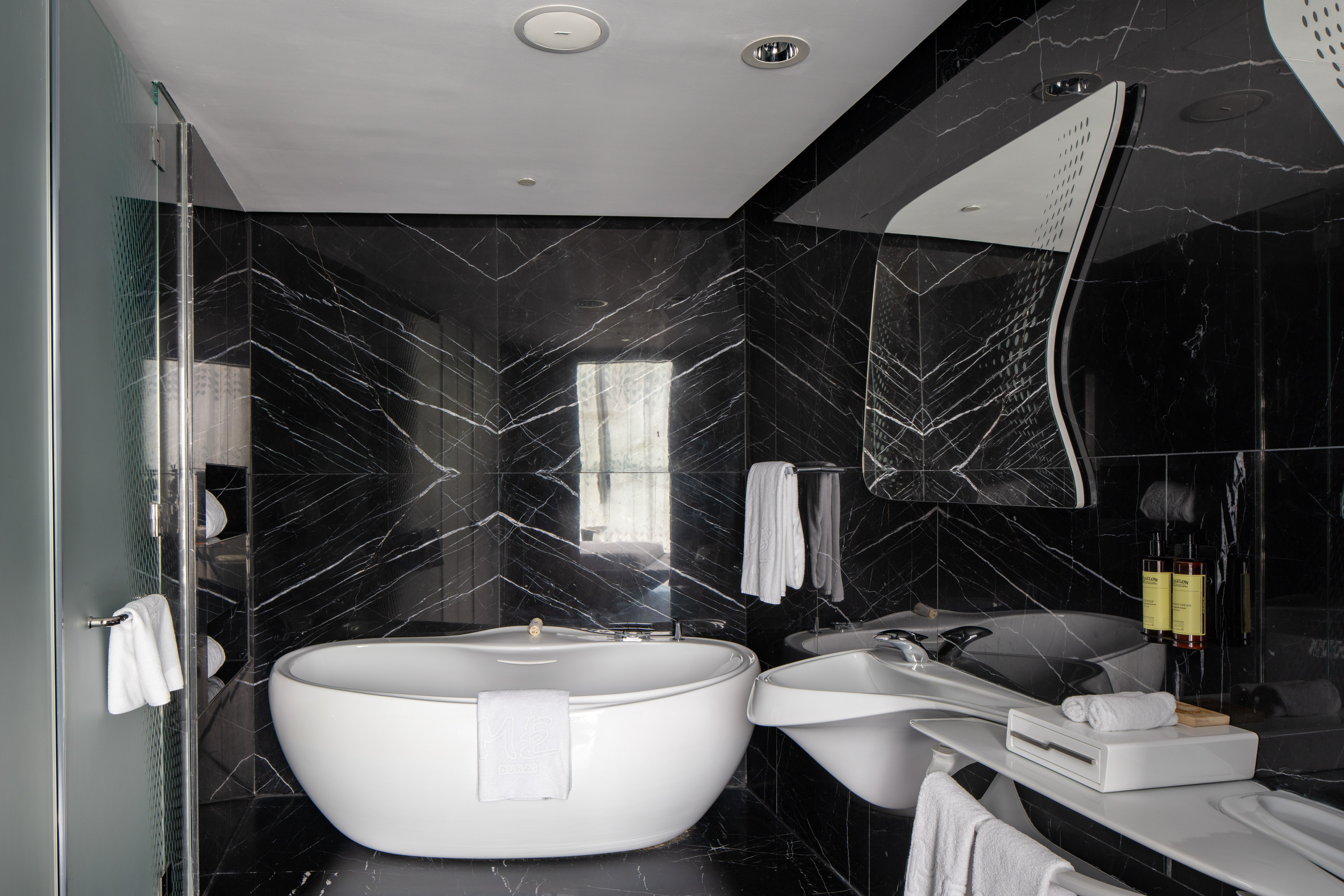 Contemporary luxury bathroom: black marble walls, white freestanding tub, glass shower.