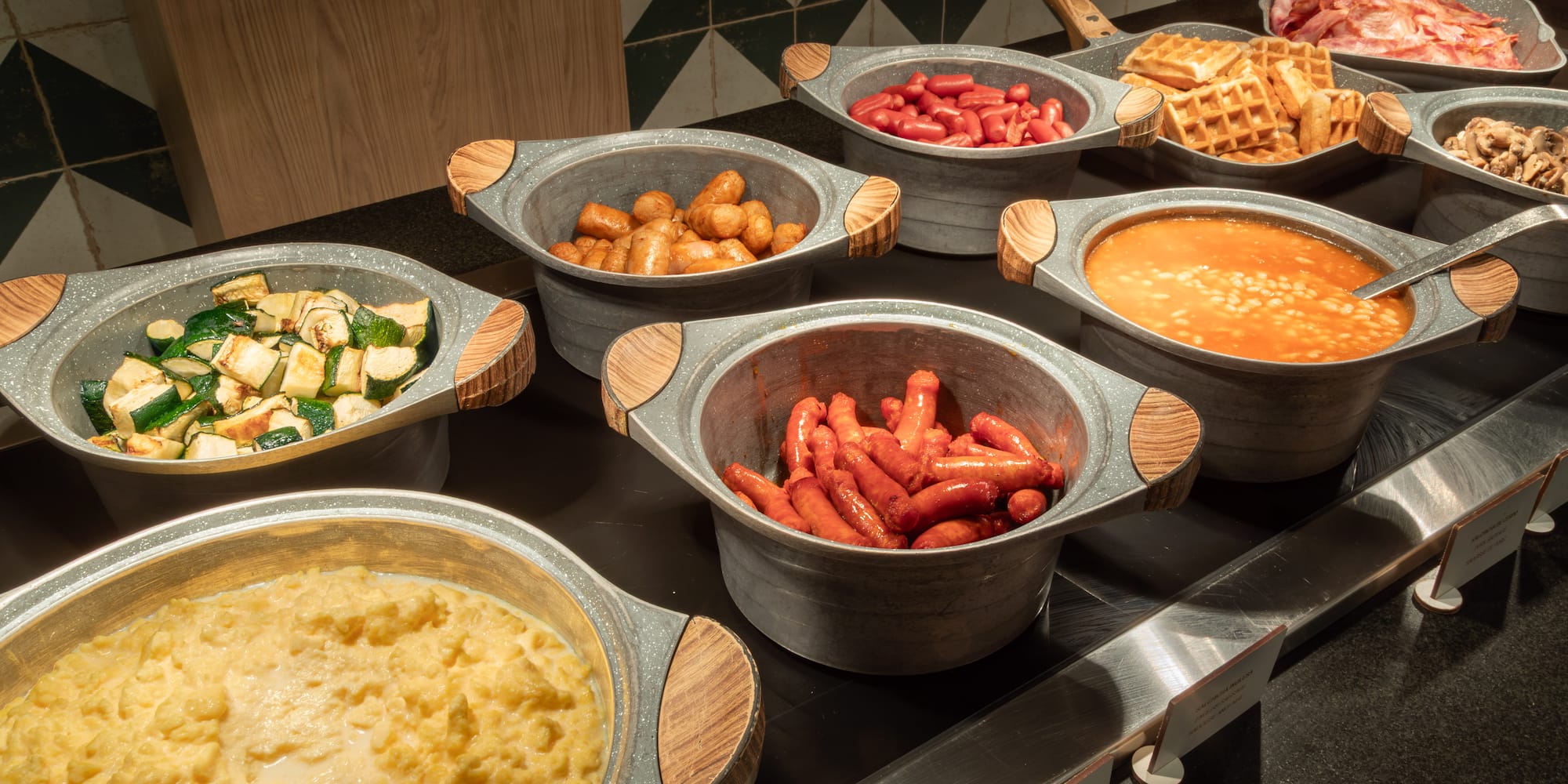 Breakfast buffet with hot eggs, bacon, waffles, baked beans, and sausages.