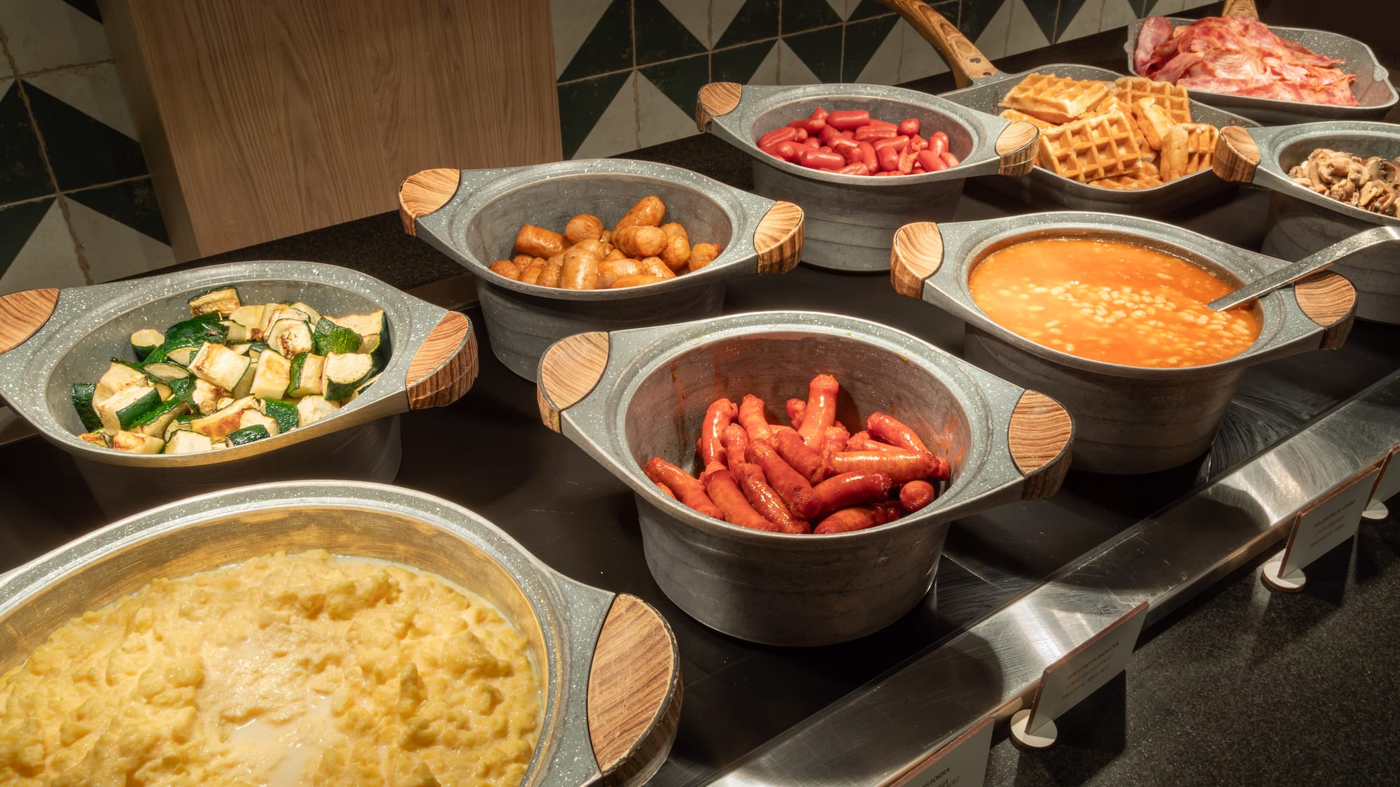 Breakfast buffet with hot eggs, bacon, waffles, baked beans, and sausages.