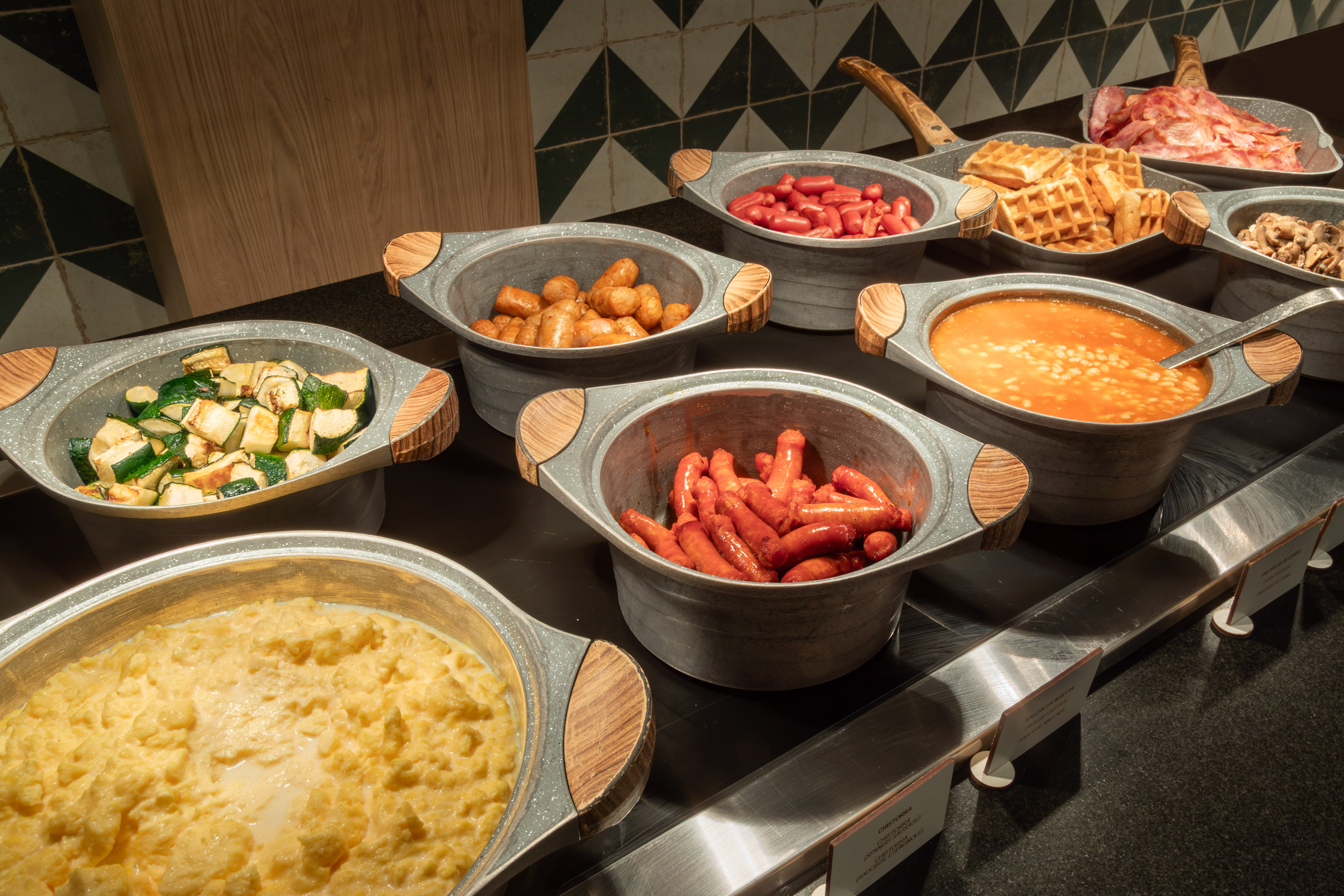 Breakfast buffet with hot eggs, bacon, waffles, baked beans, and sausages.