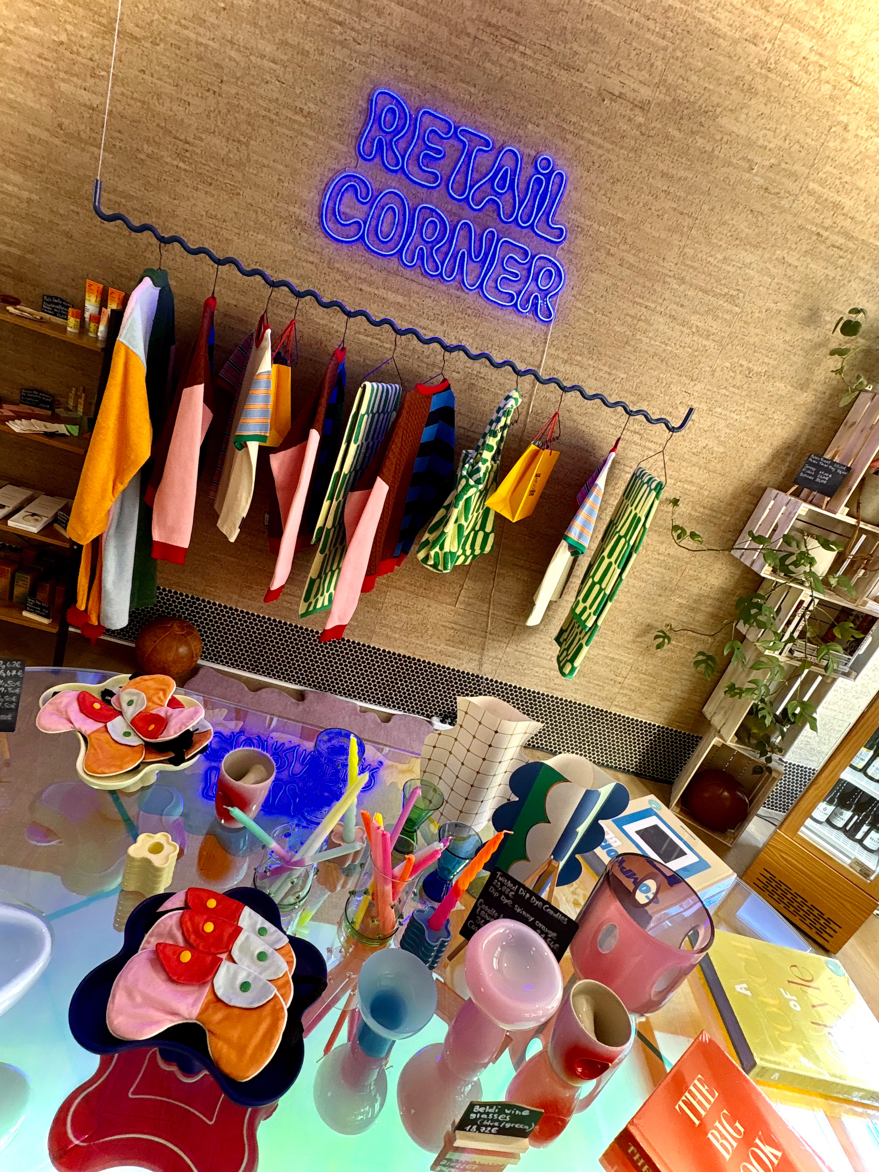 Retail corner with neon sign, colorful fashion items, and trendy home decor.
