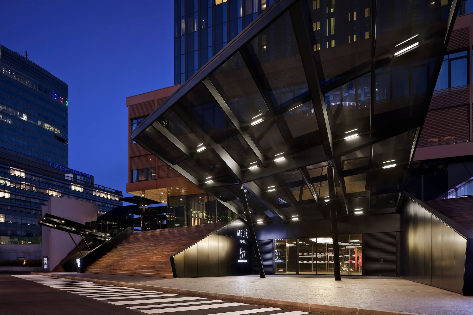 Meliá Vienna hotel exterior at dusk, modern building with illuminated entrance and stairs.