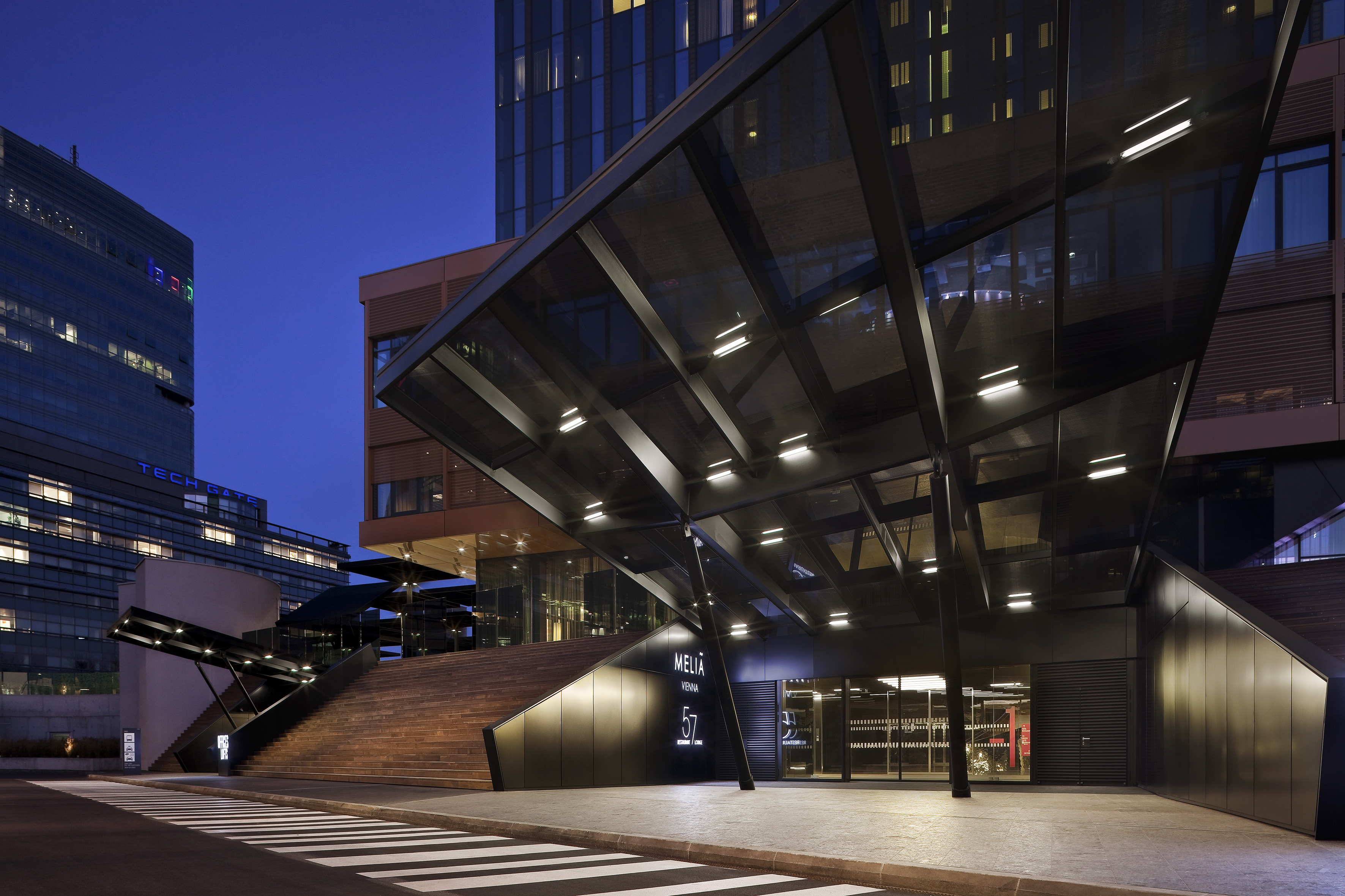 Meliá Vienna hotel exterior at dusk, modern building with illuminated entrance and stairs.