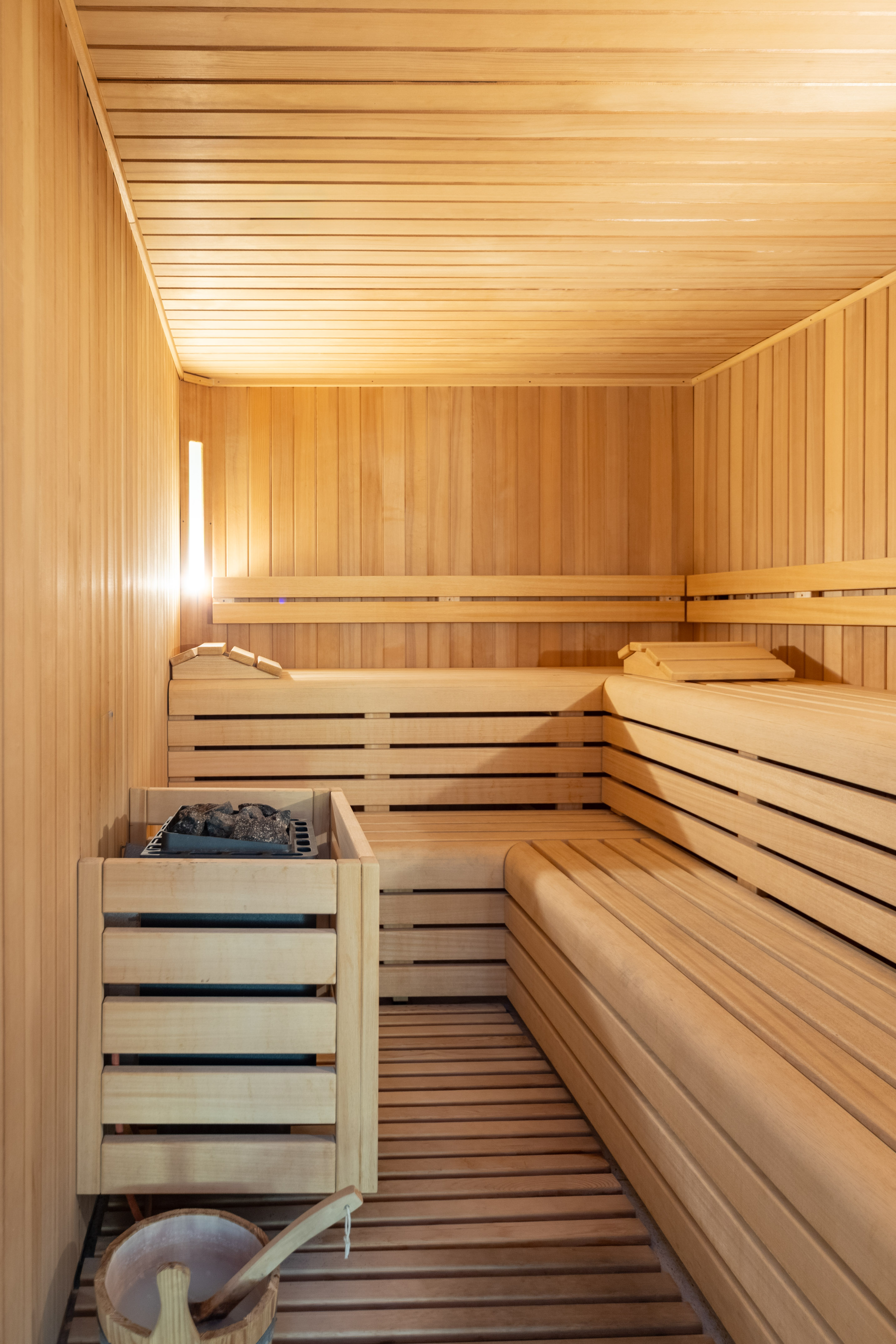 Wooden sauna room with heater, benches, bucket, and warm lighting.