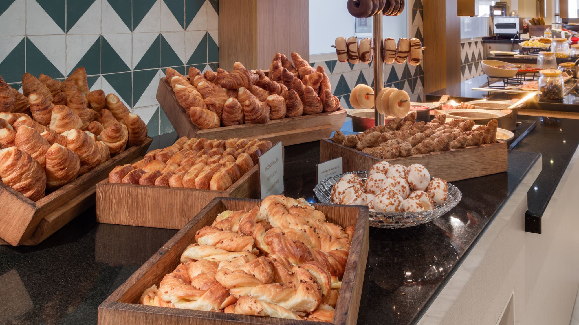 Hotel breakfast buffet with golden croissants, assorted pastries, and donuts.